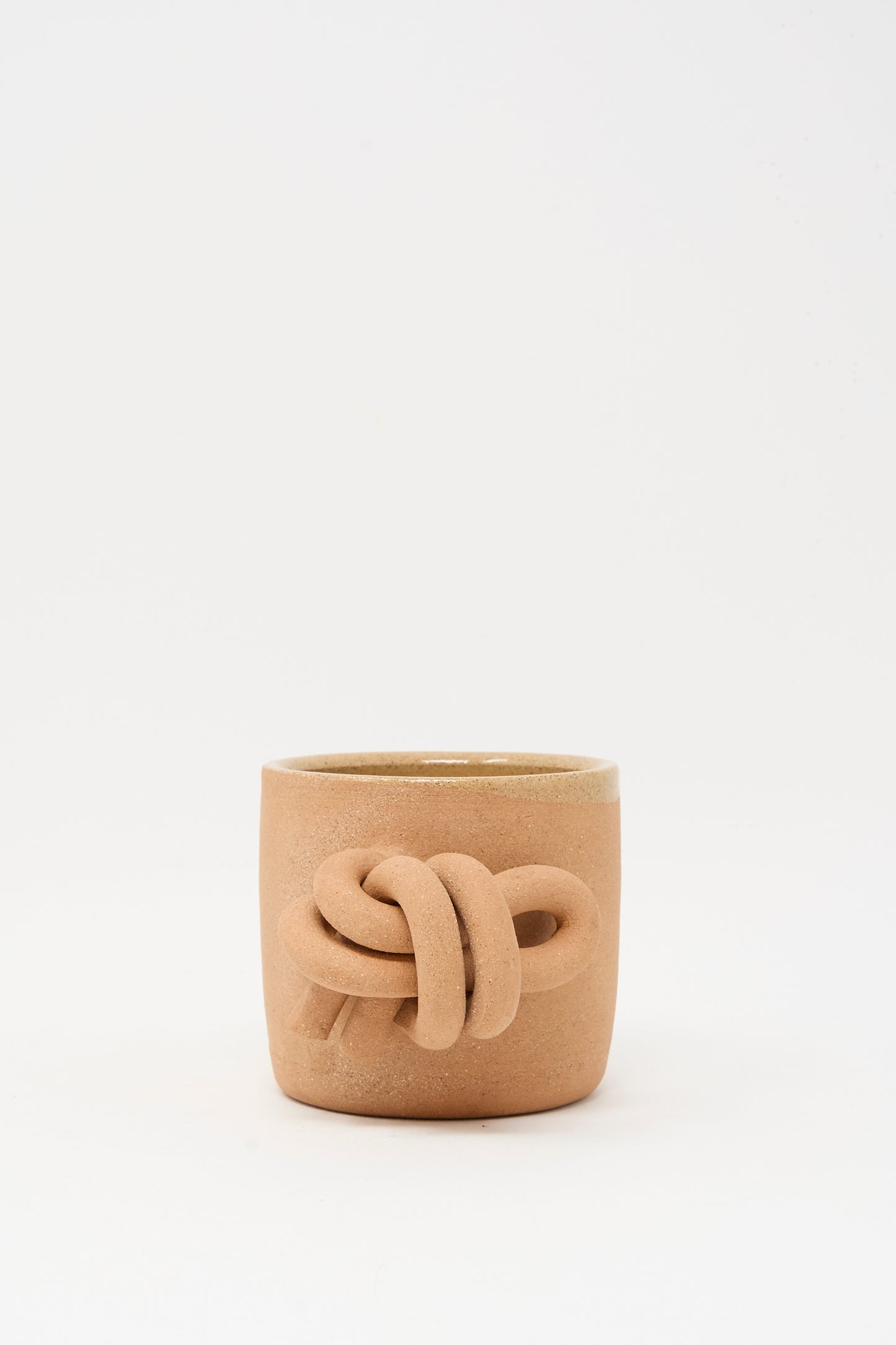 The Overhand Knot Mug in Adobe by Lost Quarry features a tan, adobe hue and a raised knot design on the front. This handmade mug is displayed against a plain white background.