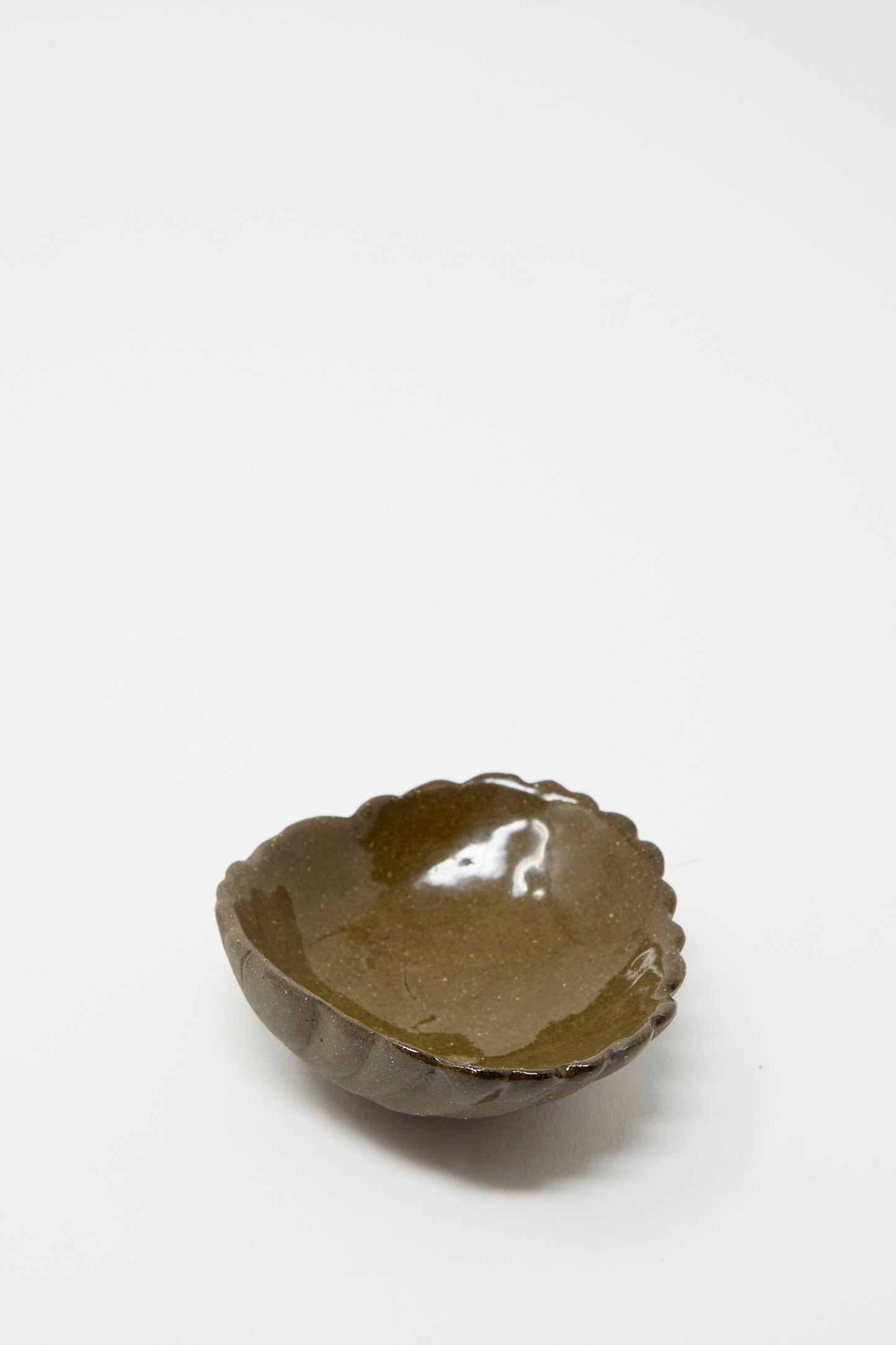 The Small Ceramic Shell Dish in Dark Brown by Lost Quarry, featuring a round shape, a scalloped edge, and a rich brown interior glaze, sits on a plain white background.