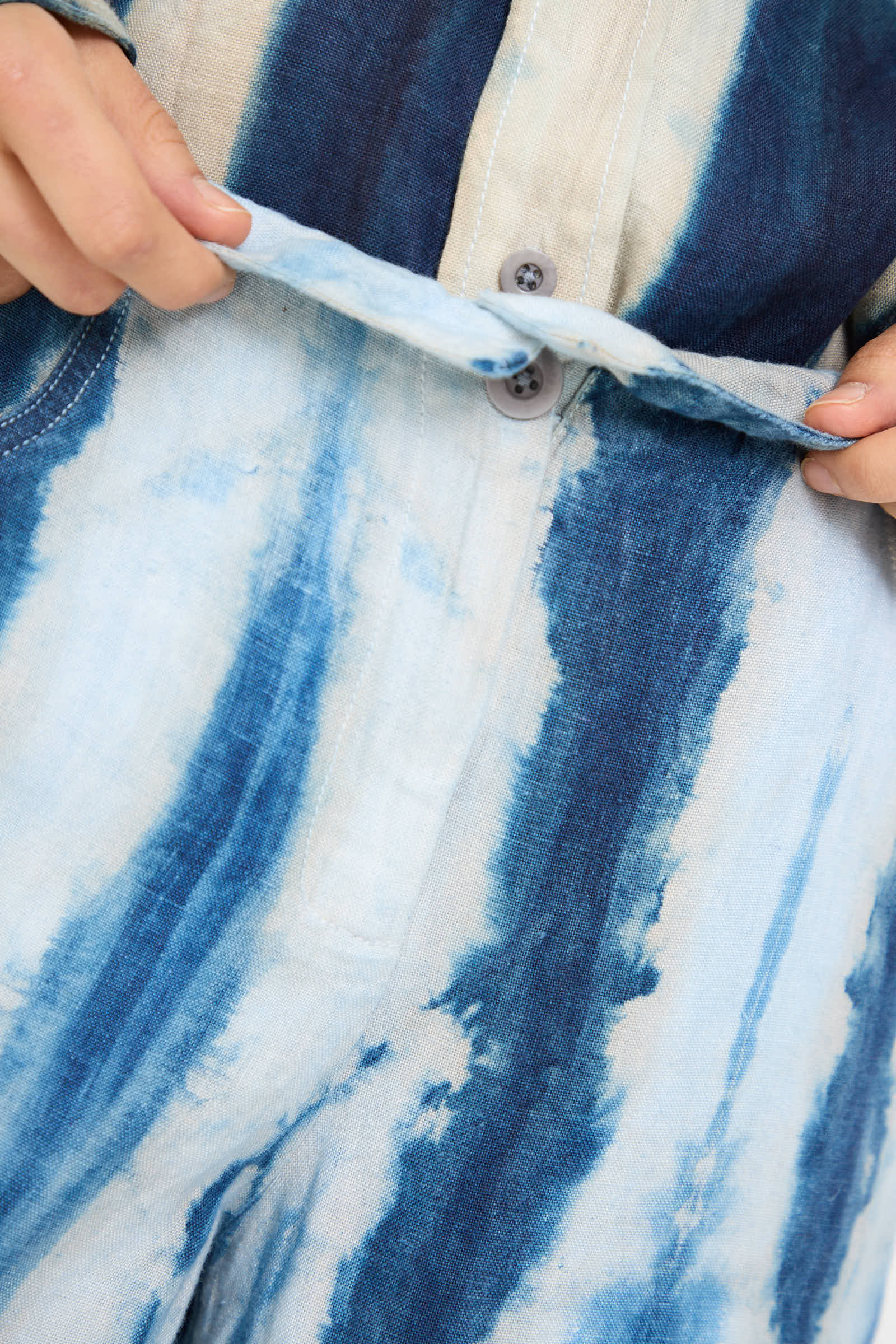 Close-up of hands holding the waistband of the Luna Del Pinal Shibori Hemp Wide Leg Trouser in Faded Indigo. The trousers feature a button closure and are crafted from sustainably grown hemp.