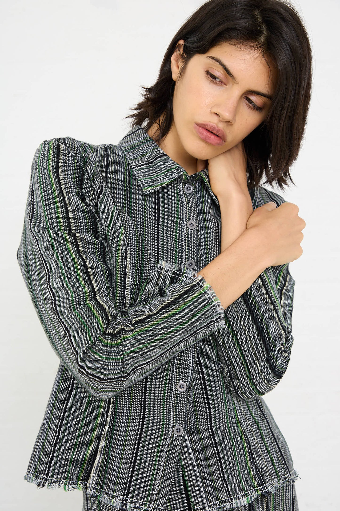 A person wearing the Luna Del Pinal Tela De Raya Loom Weave Pin Shirt in Humbug Stripe poses with one hand touching their neck against a white background.