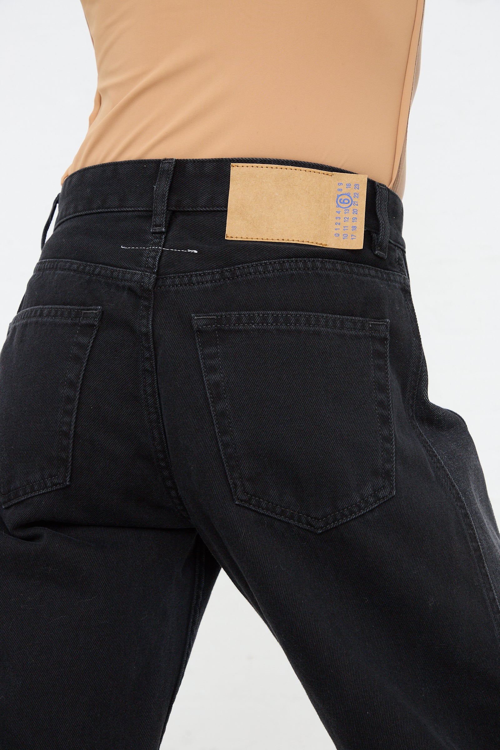 Close-up of a person wearing MM6's 5 Pocket Pant in Black with a Maison Martin Margiela beige tag on the back pocket.