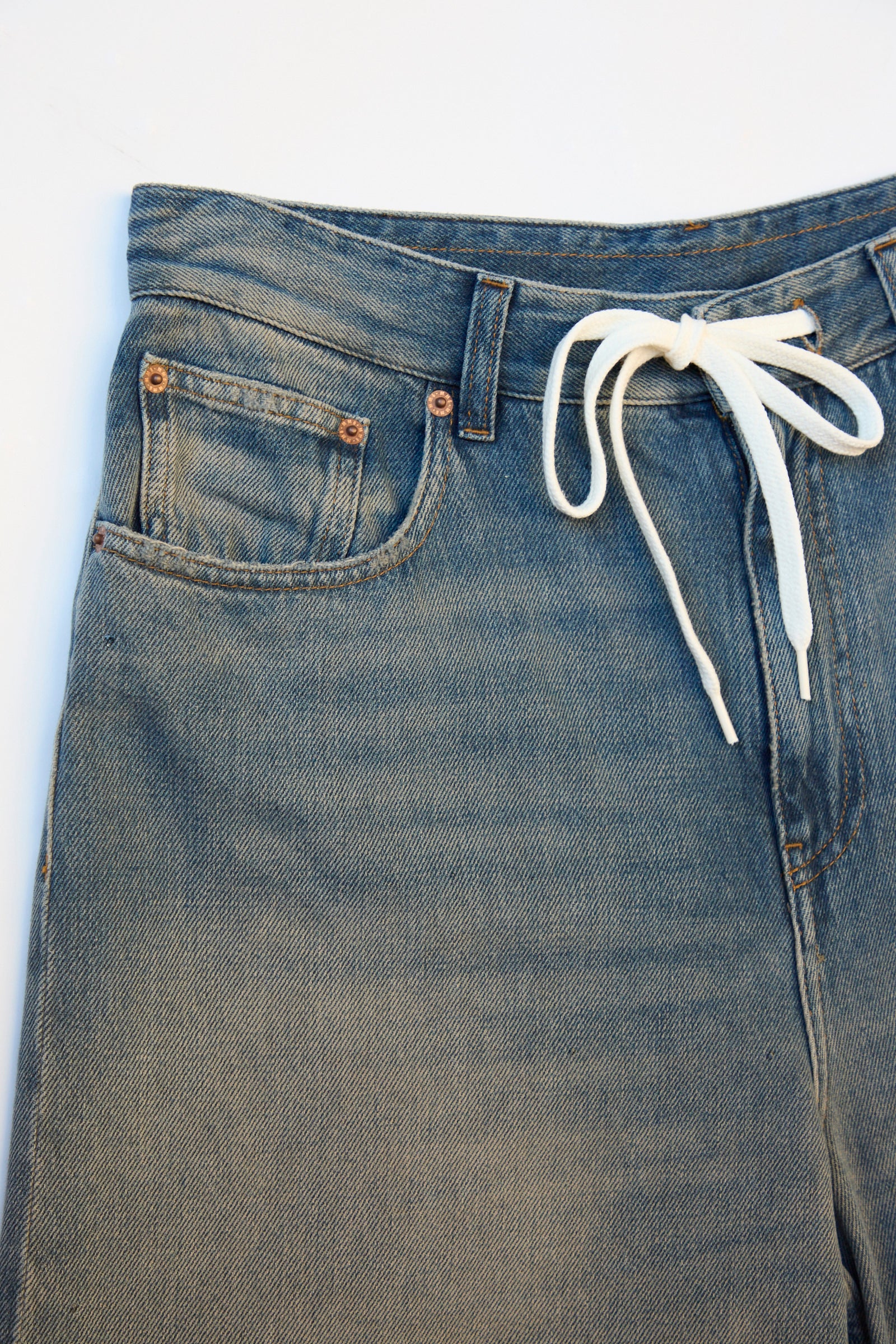 The 5 Pocket Pant in Grey Blue by MM6 is a pair of denim jeans with a high-rise style featuring a drawstring instead of a button, light blue wash, front pockets, and copper rivets.