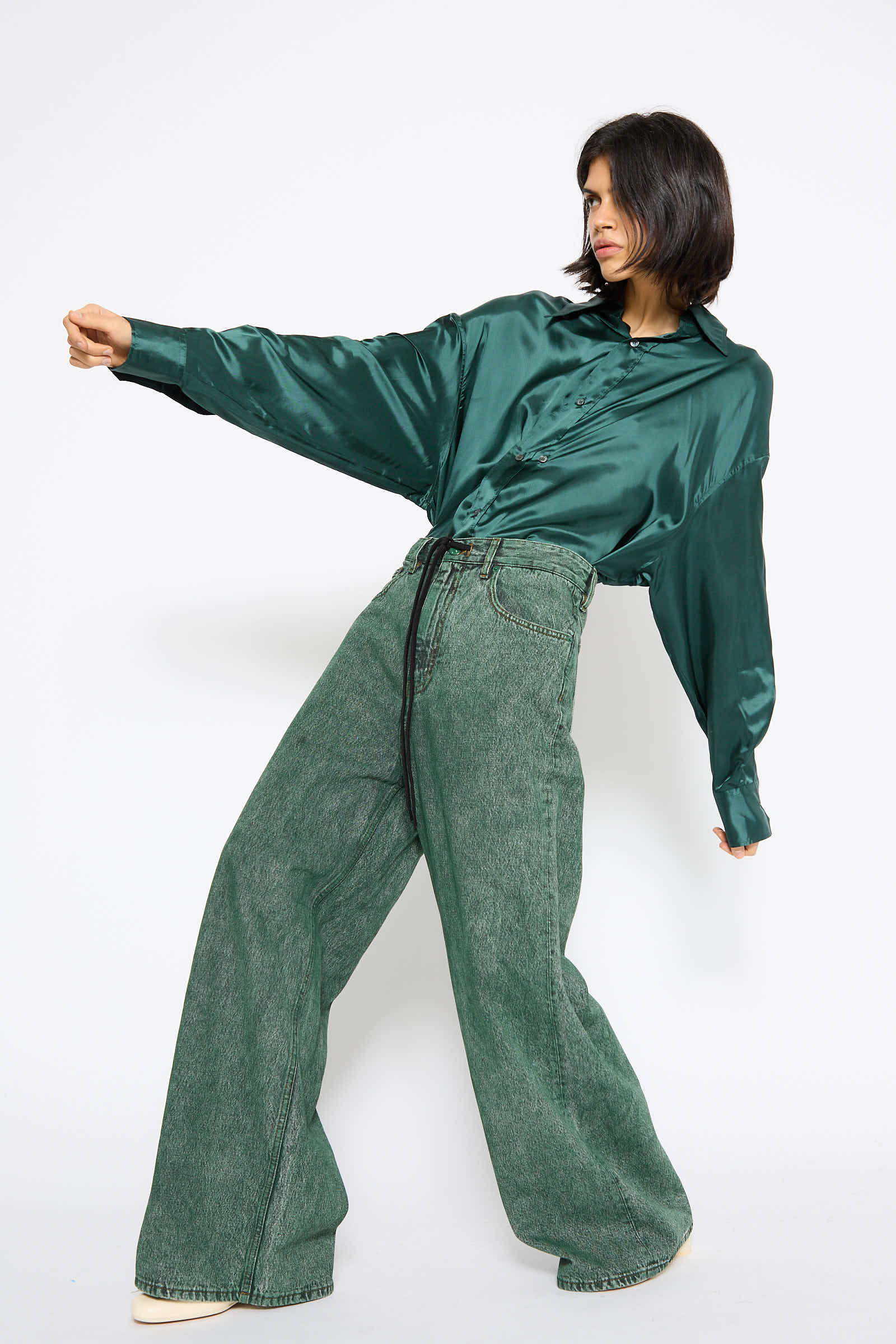 A person wearing a shiny green blouse and MM6 5 Pockets Denim Pant in Green poses against a plain white background.