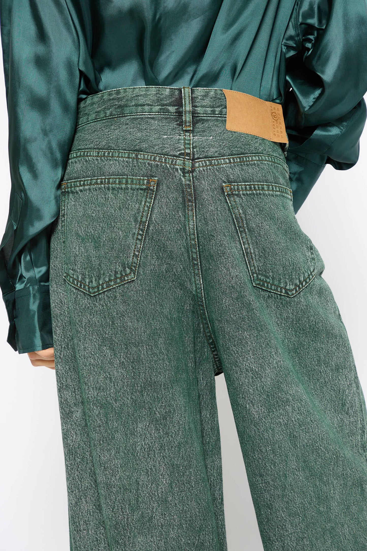 A person wearing MM6's 5 Pockets Denim Pant in Green and a green satin shirt is shown from the back. The relaxed fit jeans feature two back pockets and a brown leather patch on the waistband.