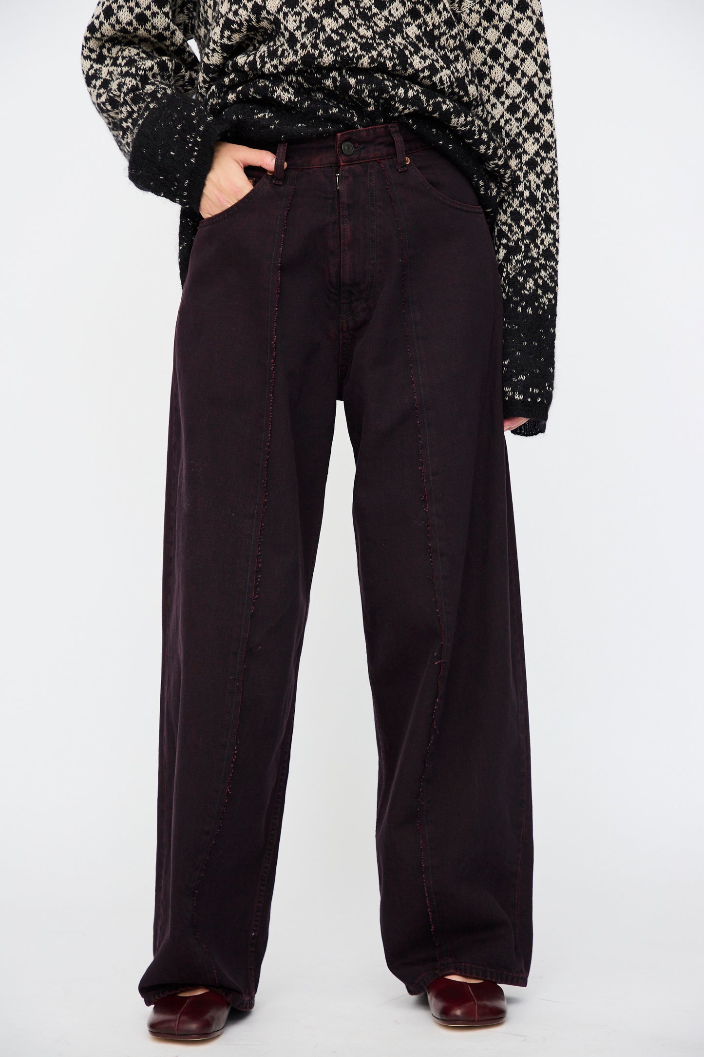 Model wearing a patterned black and white sweater, MM6 5 Pocket Pants in Burgundy with red stitching, and matching burgundy shoes, standing against a plain white background.