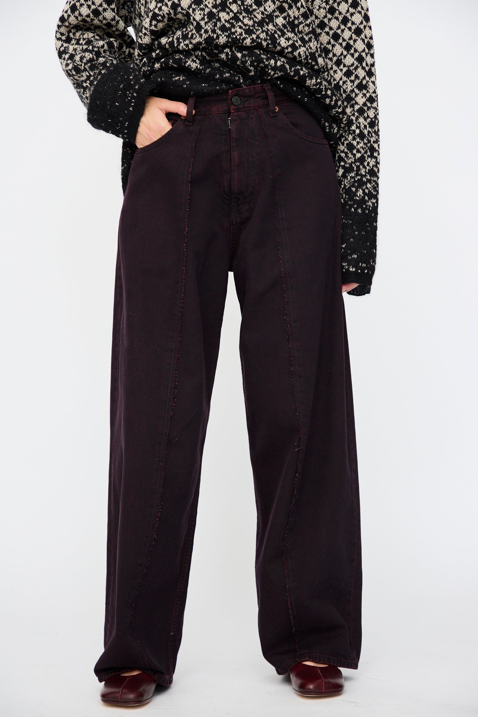 Model wearing a patterned black and white sweater, MM6 5 Pocket Pants in Burgundy with red stitching, and matching burgundy shoes, standing against a plain white background.