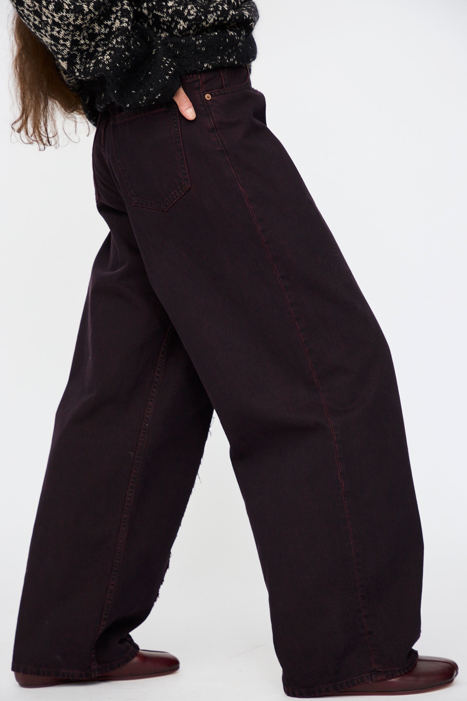 A person is wearing MM6's 5 Pocket Pants in Burgundy with a black patterned sweater and brown shoes, photographed from the side against a plain background.