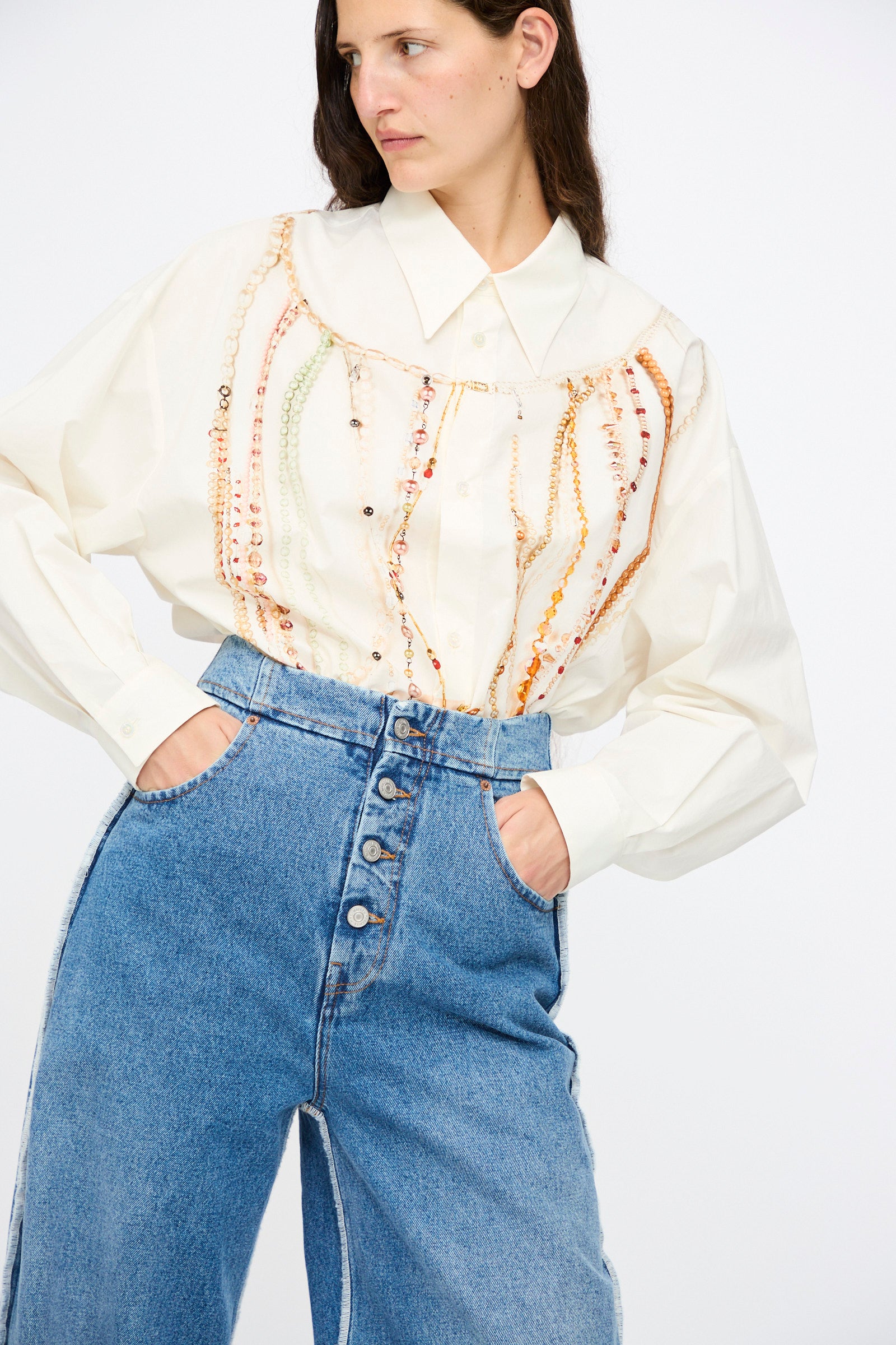 A woman wearing a cream blouse with decorative beading and MM6 5 Pocket Pants in Medium Blue stands against a plain white background.