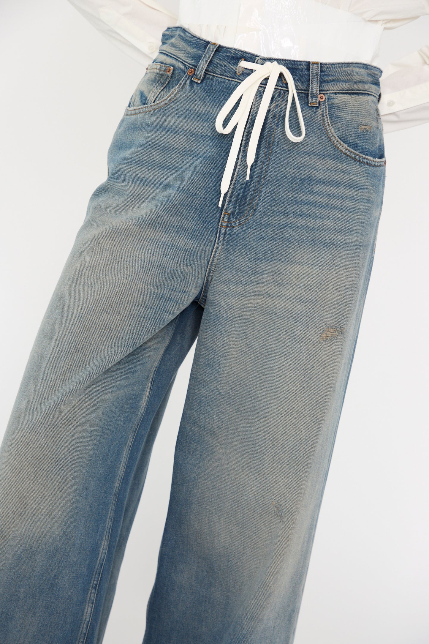 The 5 Pocket Pant in Grey Blue by MM6, featuring a white drawstring at the waist, is showcased elegantly on a clear mannequin.