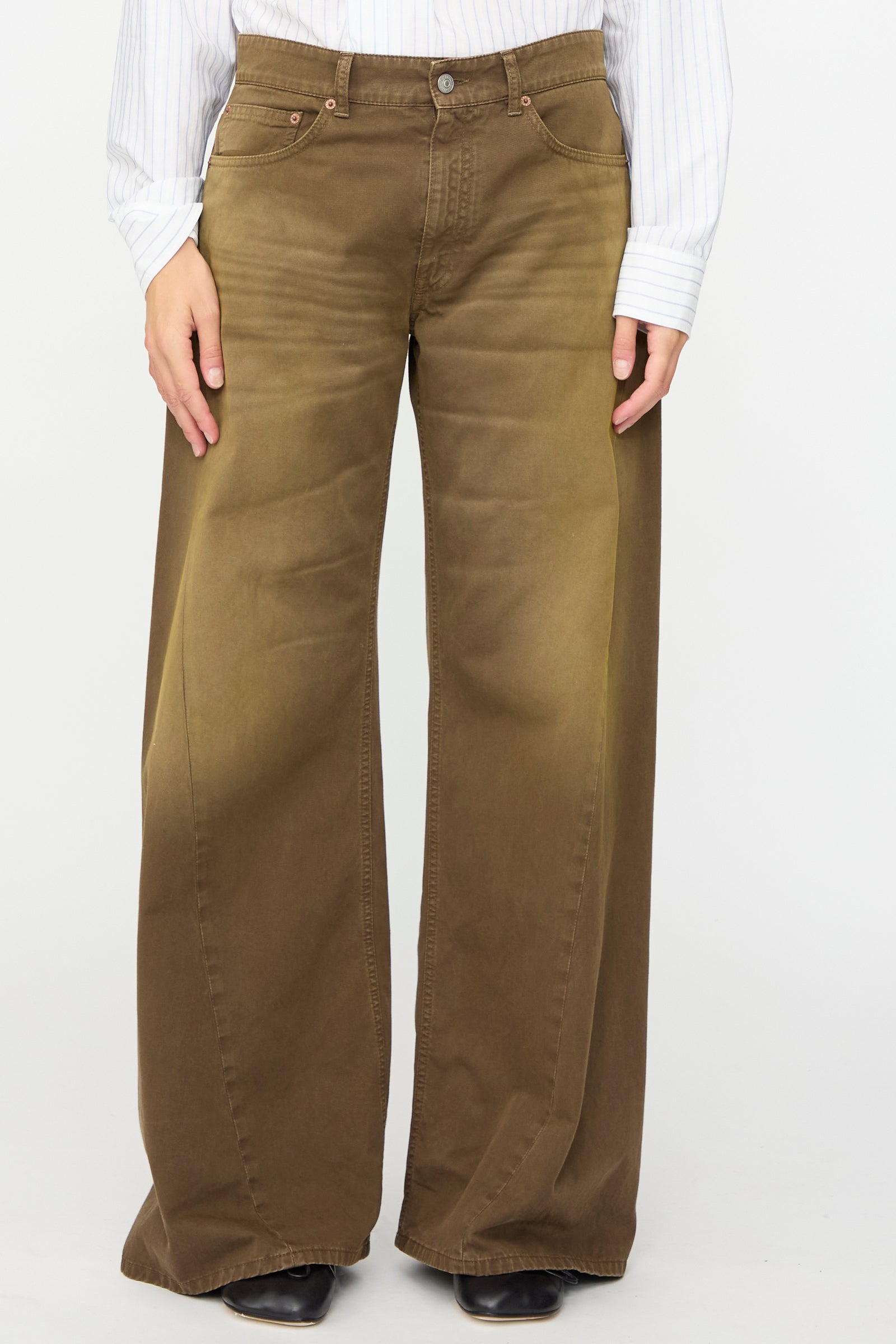 A person wearing a white long-sleeve shirt and the MM6 5 Pockets Pants in Brown, featuring a relaxed fit and wide leg cut in cotton twill denim, stands against a plain background.