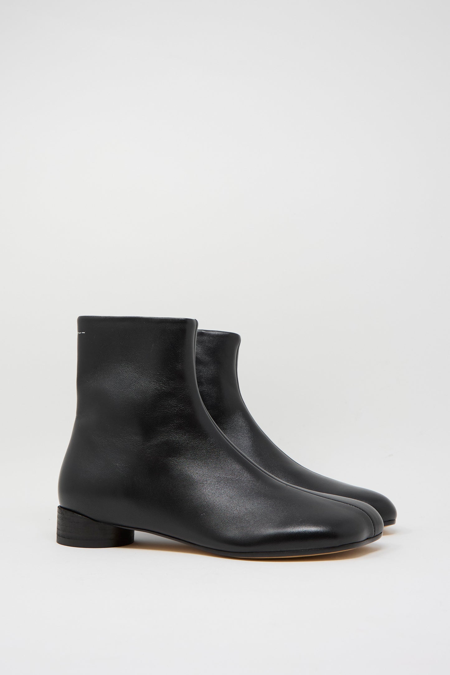 The MM6 Ankle Boot in Black is made in Italy from calfskin leather, featuring a minimalist design with a slight heel.