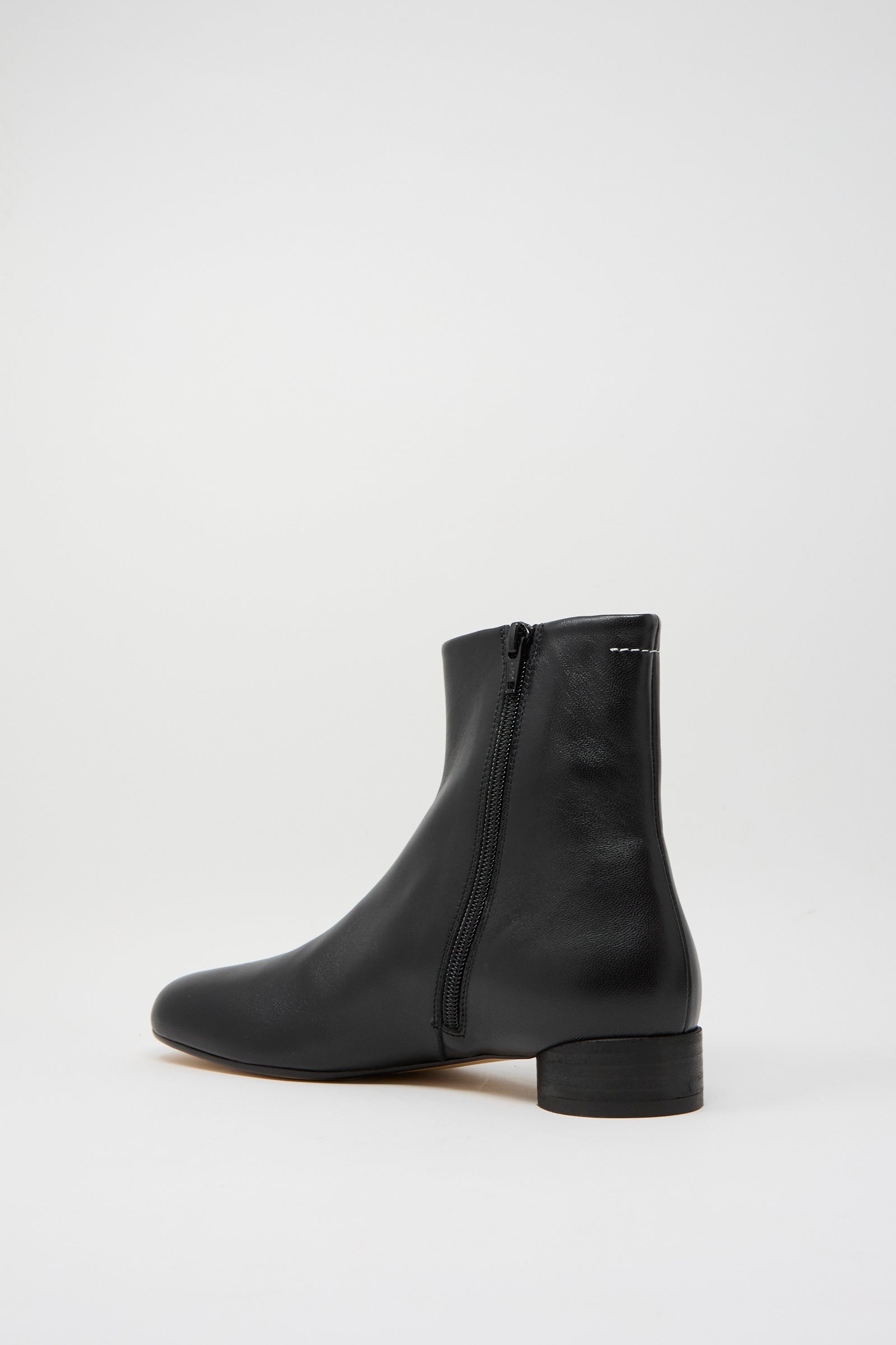 The "Ankle Boot in Black" by MM6 is a black ankle boot made from calfskin leather, complete with a side zipper and low heel, showcased against a simple white backdrop.