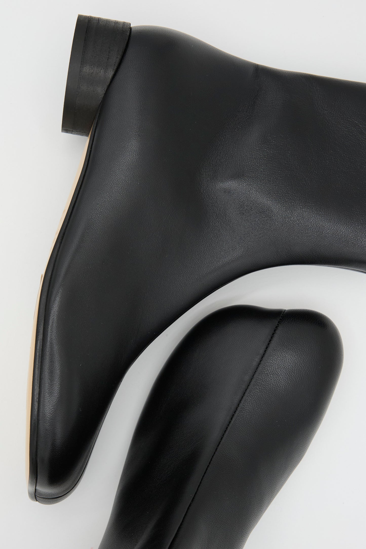 Close-up of two black ankle-high boots from MM6, known as the Ankle Boot in Black, made from calfskin leather. They are displayed from the side and top view on a white background.