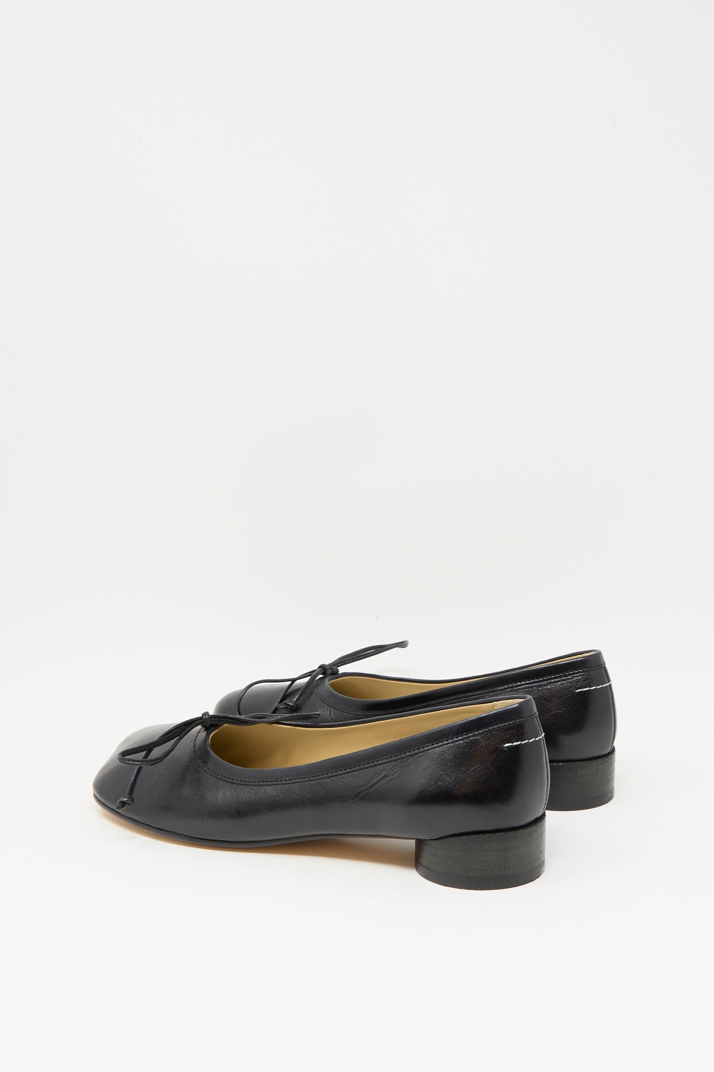 The MM6 Ballet Shoe in Black is crafted from calf leather, features small heels and bow accents, and is made in Italy; it is shown on a plain white background.