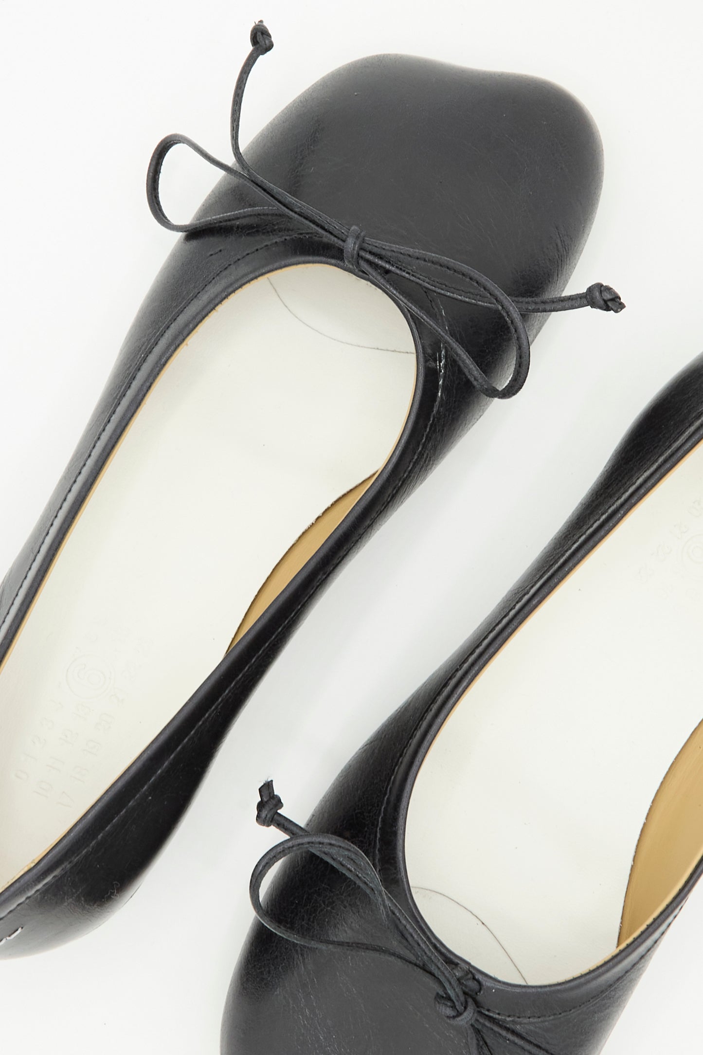 The Ballet Shoe in Black by MM6, crafted from black calf leather and featuring front bows, is made in Italy and displayed from above on a white background.