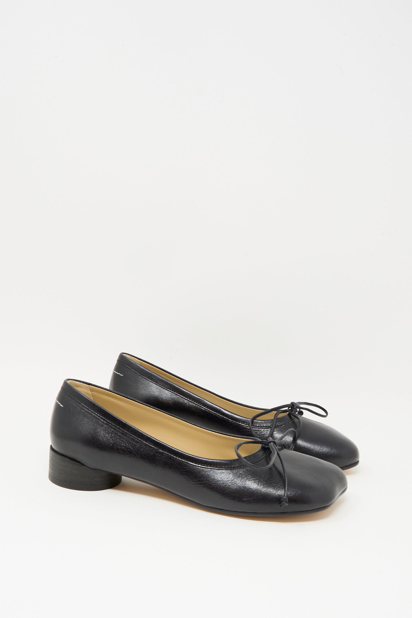 The MM6 Ballet Shoe in Black is crafted from calf leather and features low heels with delicate bow accents on the front; made in Italy, it is shown against a plain white background.