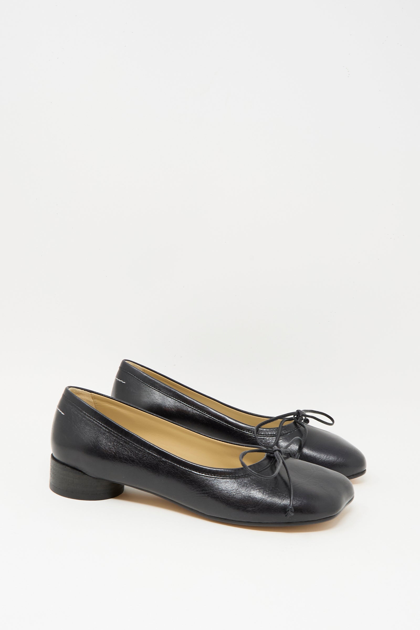 The MM6 Ballet Shoe in Black is crafted from calf leather and features low heels with delicate bow accents on the front; made in Italy, it is shown against a plain white background.
