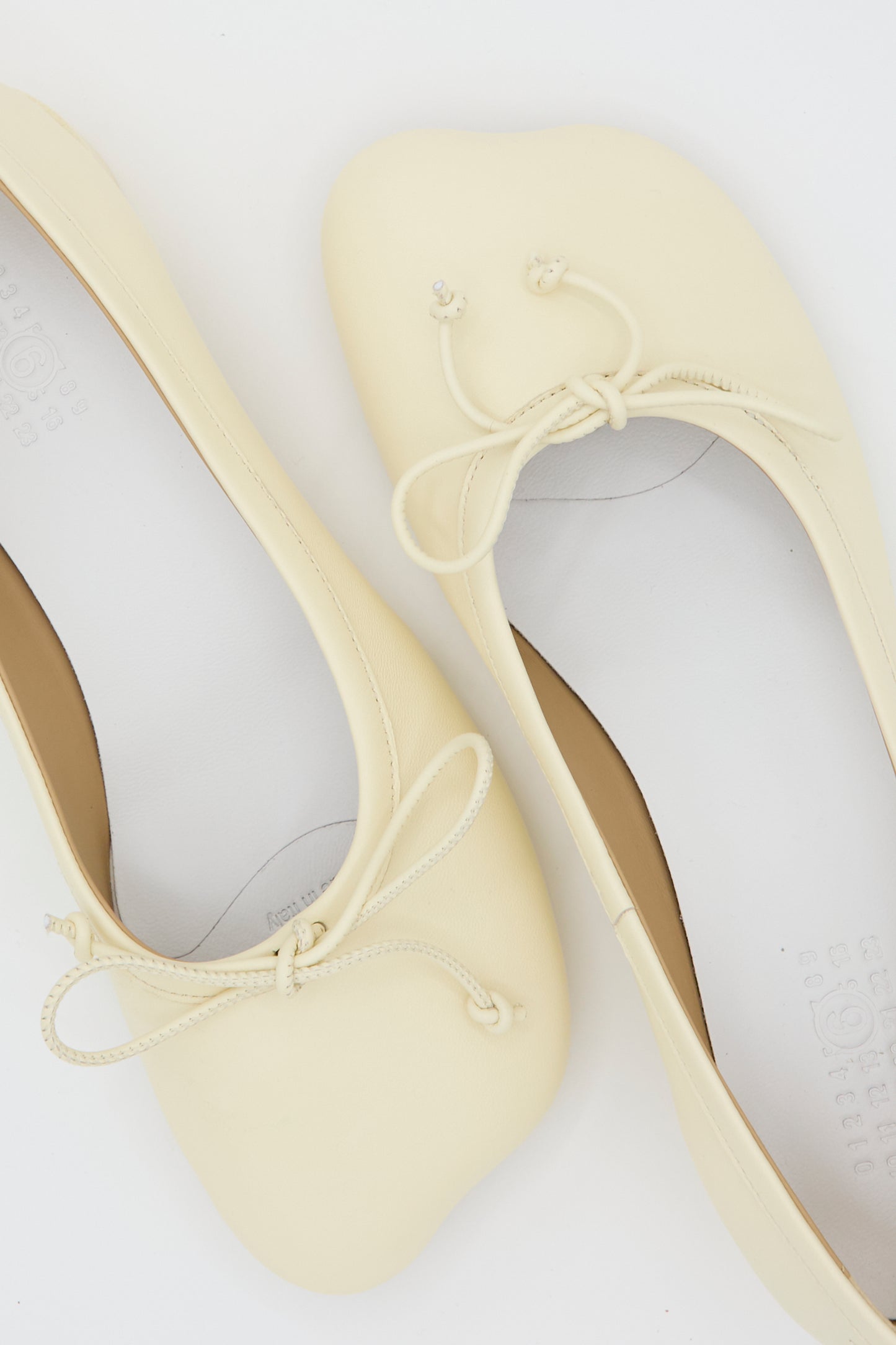 A pair of MM6 Ballet Shoes in Cream, featuring rounded toes and front bows, displayed on a white background.