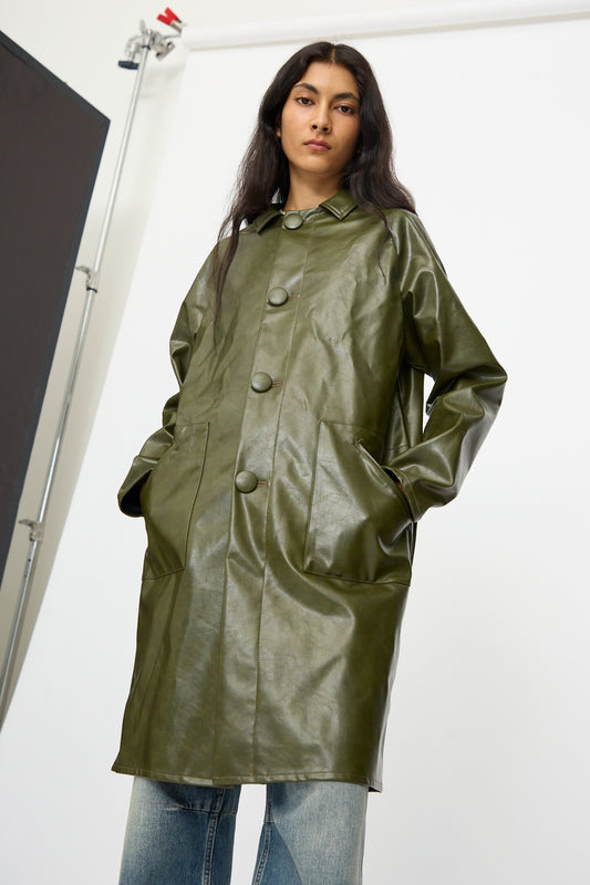 A person stands with hands in pockets, modeling the MM6 Coat in Forest Green with blue jeans against a plain studio backdrop.