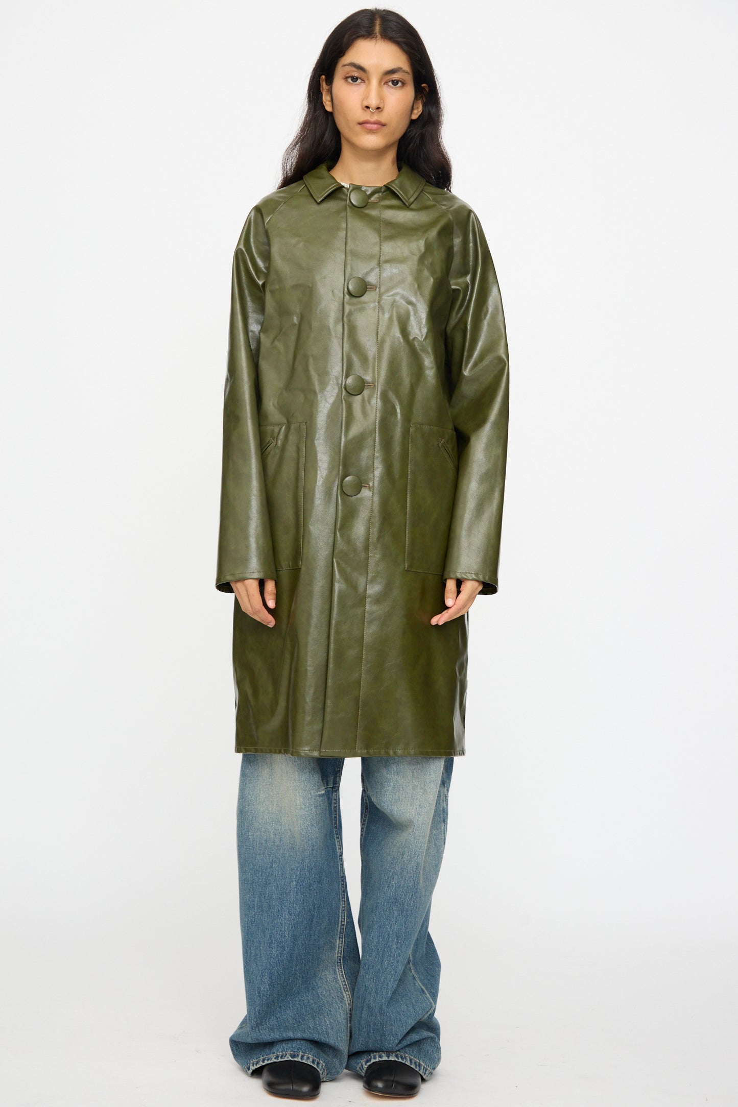 A person wears the MM6 Coat in Forest Green over wide-leg blue jeans and black shoes, standing against a plain white background.