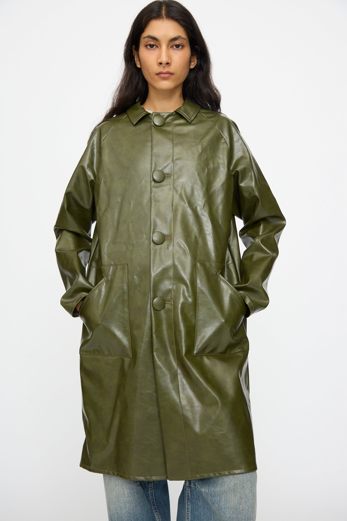A model wears the MM6 Coat in Forest Green—a button-up, faux leather piece with large front pockets—standing against a plain background.