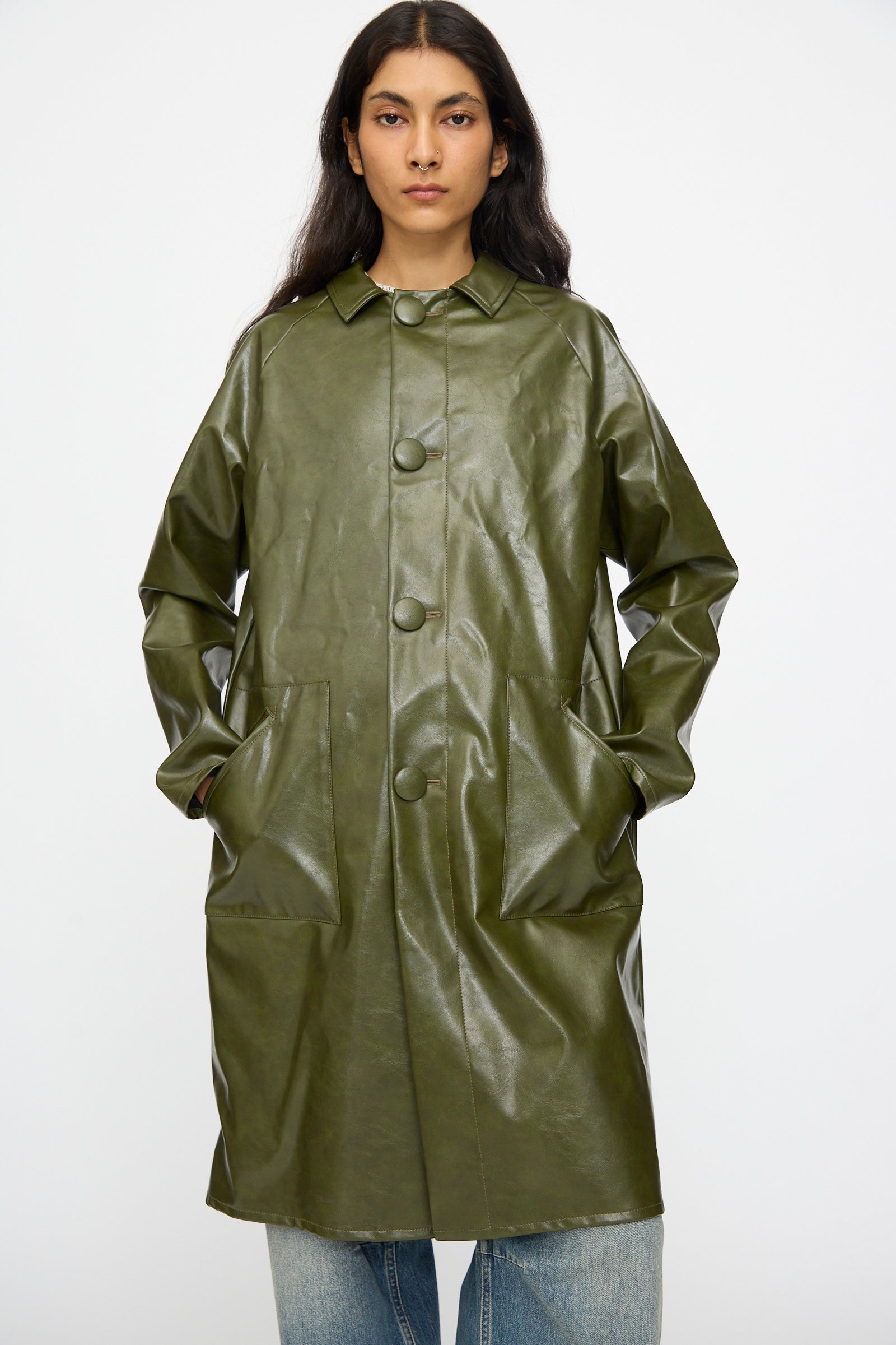 A model wears the MM6 Coat in Forest Green—a button-up, faux leather piece with large front pockets—standing against a plain background.