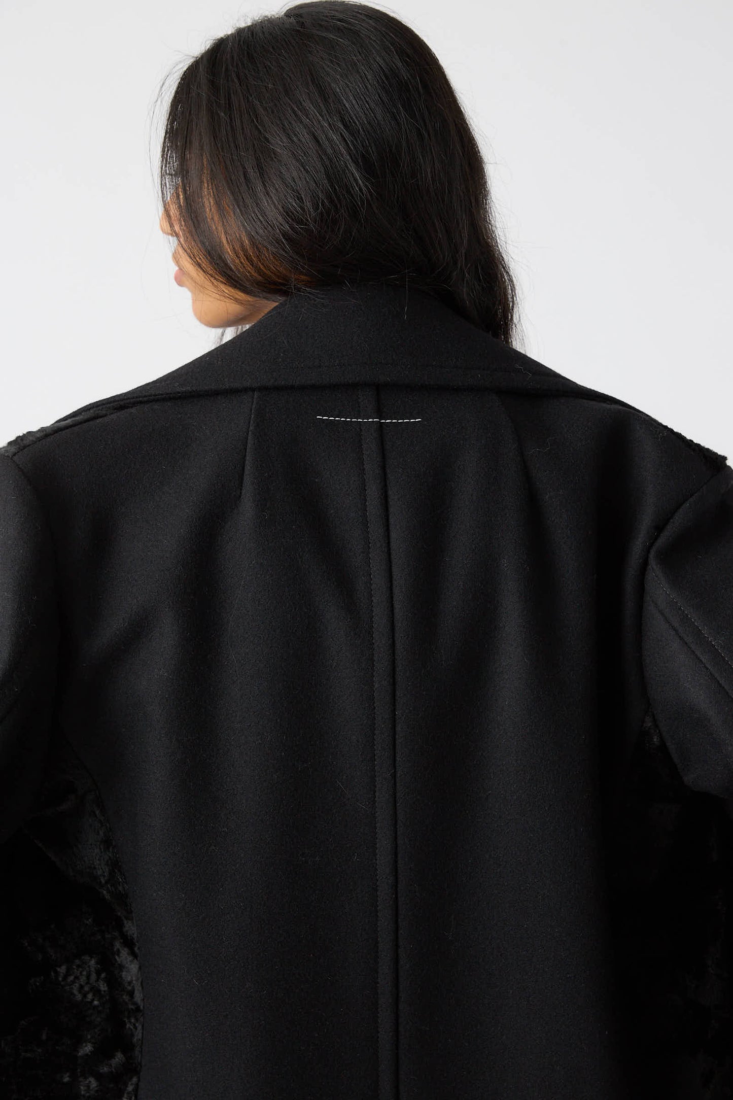 A person with long dark hair seen from the back, wearing the MM6 Coat in Black with broad lapels and the collar turned up.