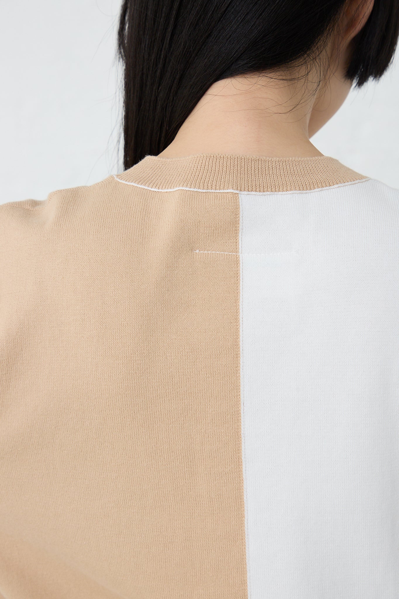 The back view of a woman wearing a relaxed fit, bi-color Crewneck in Beige Off White cotton sweater with a crew neck by MM6.