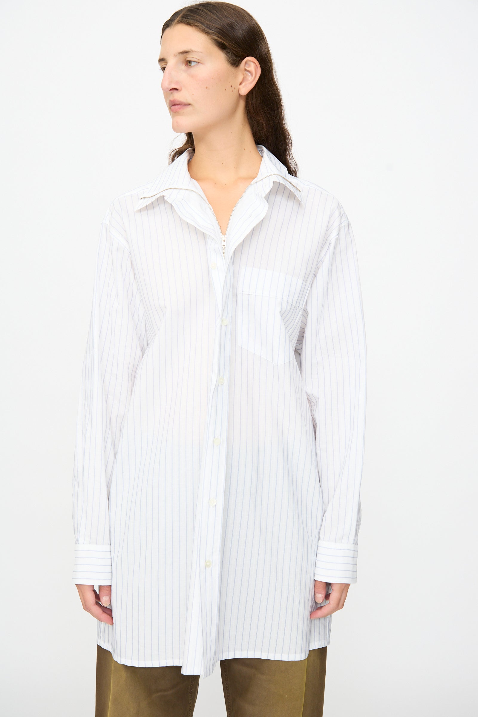 A person wears the MM6 Long-Sleeved Shirt in White and Blue—crafted from 100% cotton in Italy—paired with brown pants, standing against a plain white background.