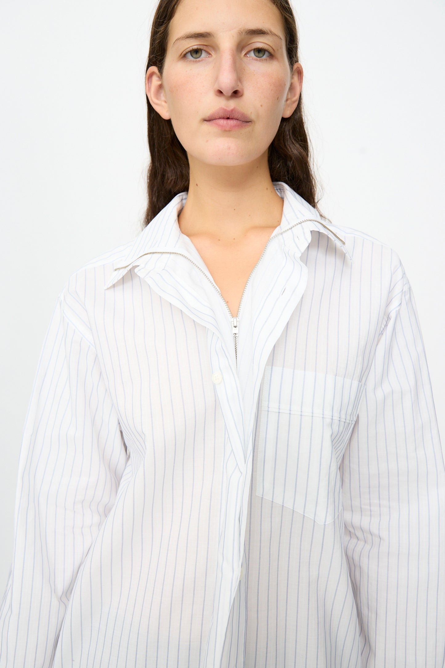 A person with long brown hair wears the MM6 Long-Sleeved Shirt in White and Blue, styled over a white top, standing against a plain light background.