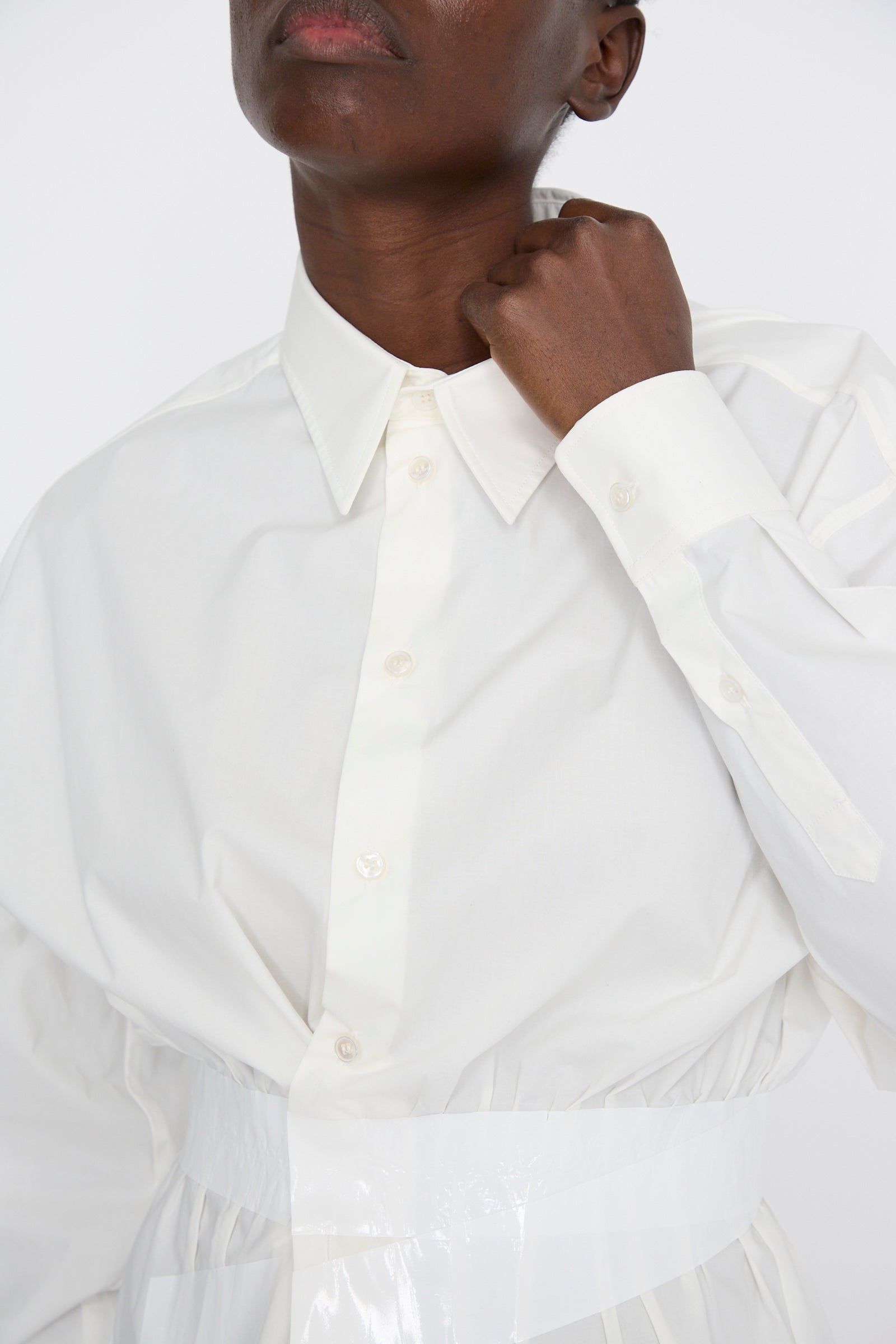 With one hand adjusting the collar, a person showcases the elegant button-up design of the MM6 Long Sleeve Shirt in Off White, featuring a relaxed fit and cotton poplin fabric.