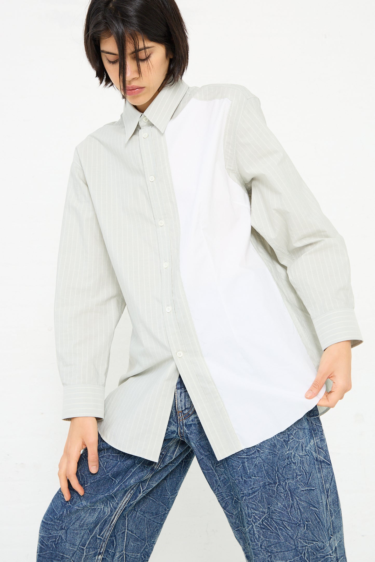 Person wearing a mismatched MM6 Long Sleeved Shirt in Iguana with light-colored and white panels and a pair of textured blue jeans, posing against a plain white background.