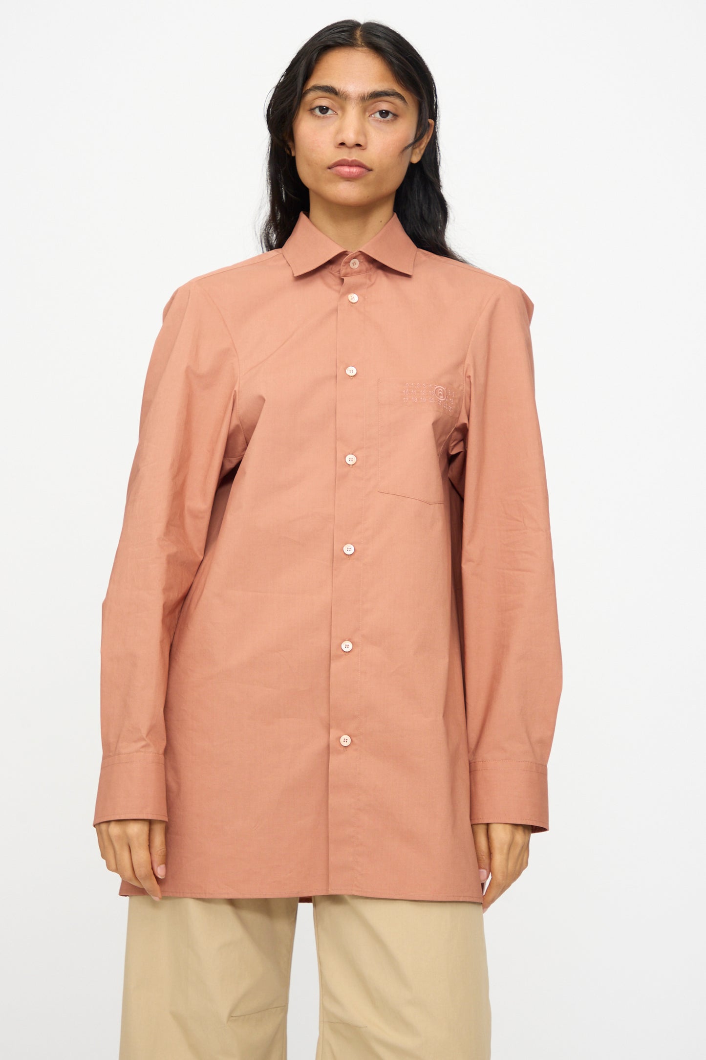 Model wears the MM6 Long Sleeved Shirt in Terracotta Red with beige pants, standing against a plain white background.