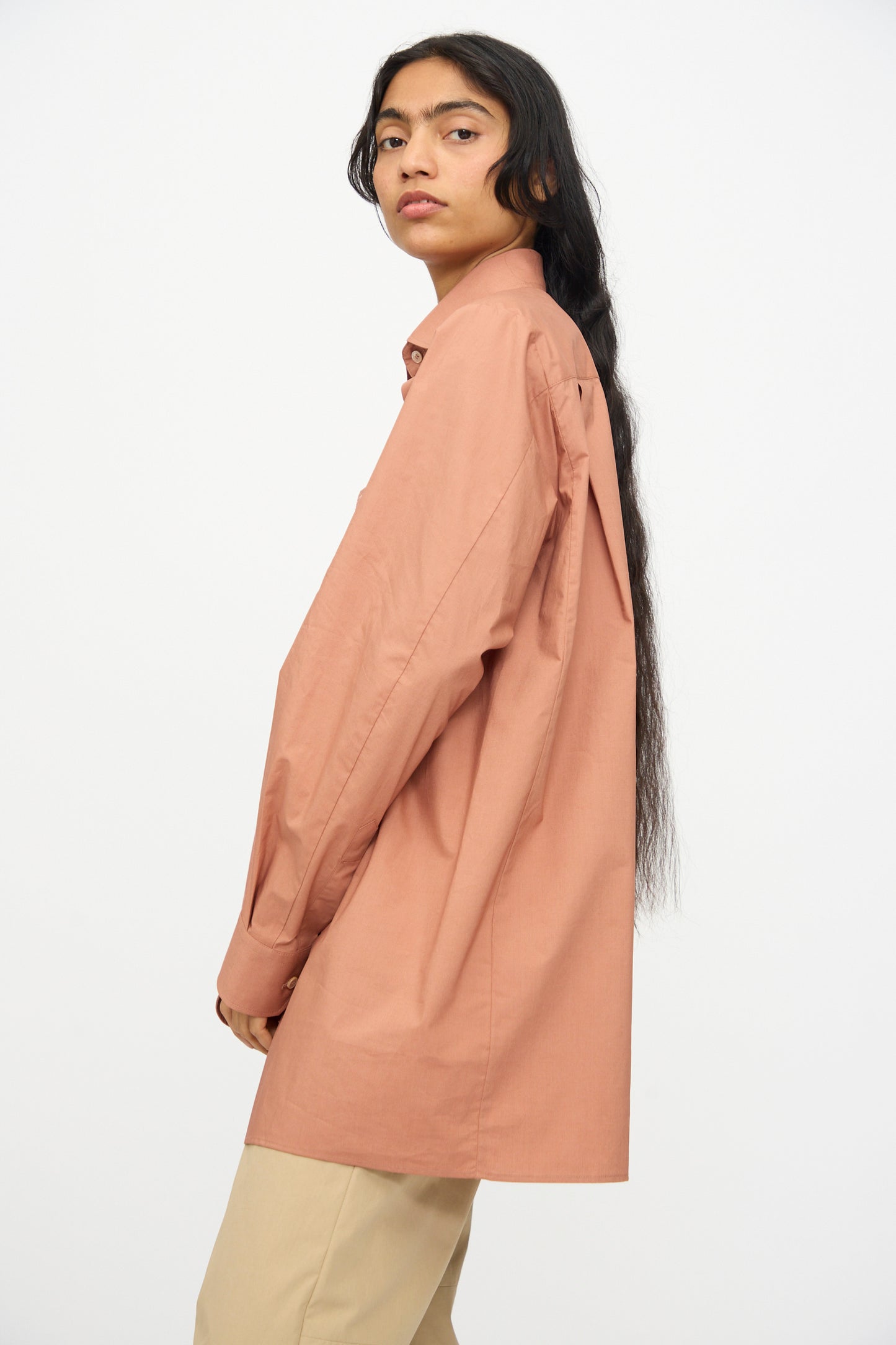 A person with long dark hair wears the MM6 Long Sleeved Shirt in Terracotta Red and beige pants, standing against a plain white background.