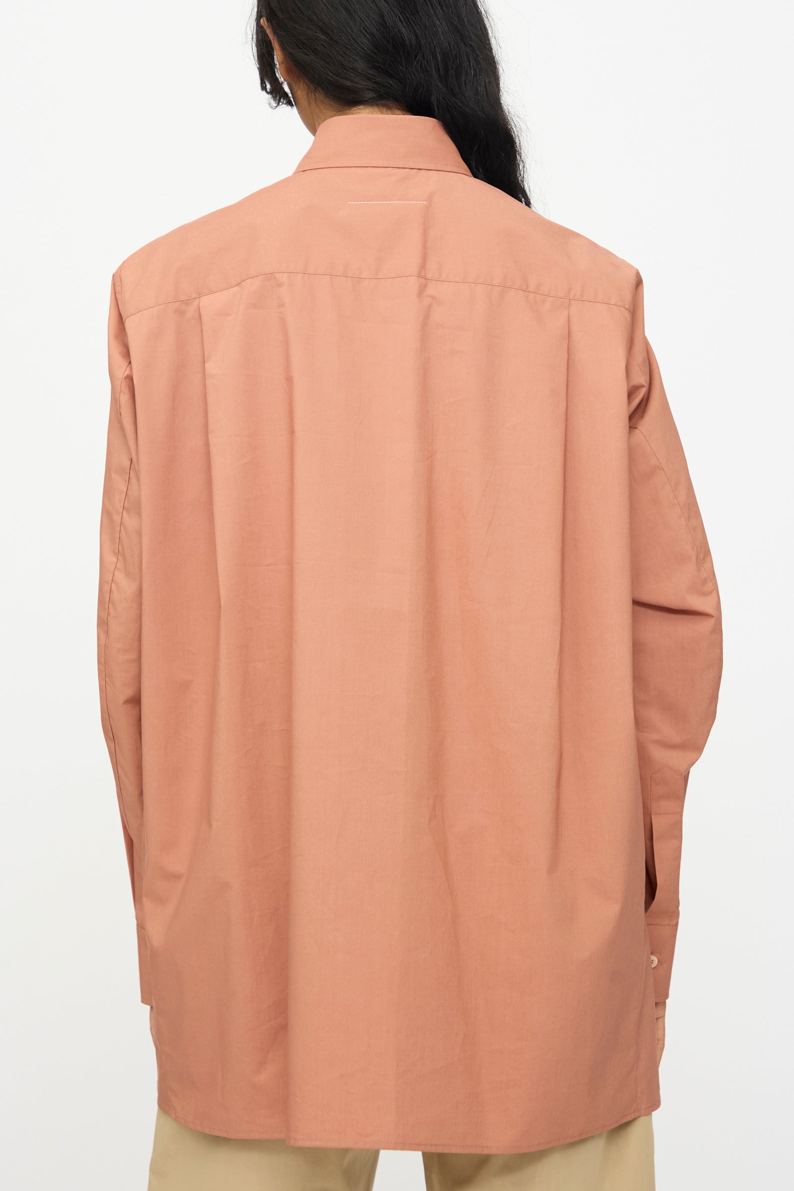 Person shown from the back wearing MM6's relaxed fit, long sleeved shirt in Terracotta Red with beige pants against a plain background.