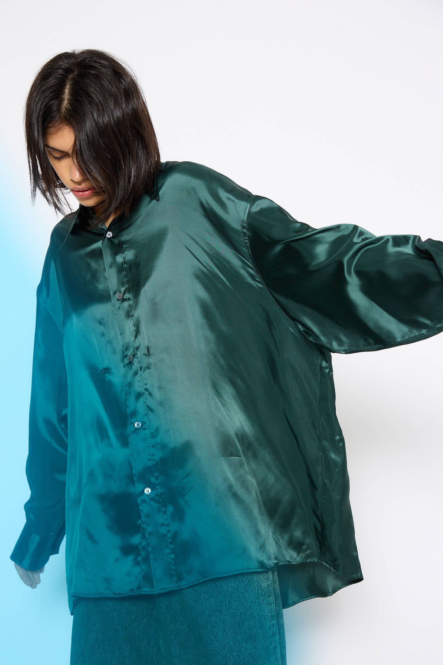 A person is wearing an oversized Long Sleeved Shirt in Green by MM6, paired with blue jeans, standing against a white background.