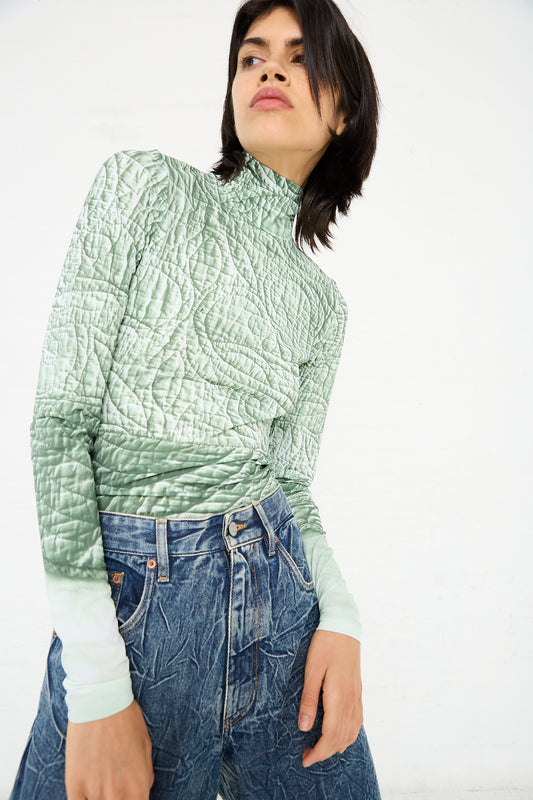 Person standing against a white background, wearing an MM6 Long Sleeved Top in Iguana and high-waisted blue jeans with a star pattern.