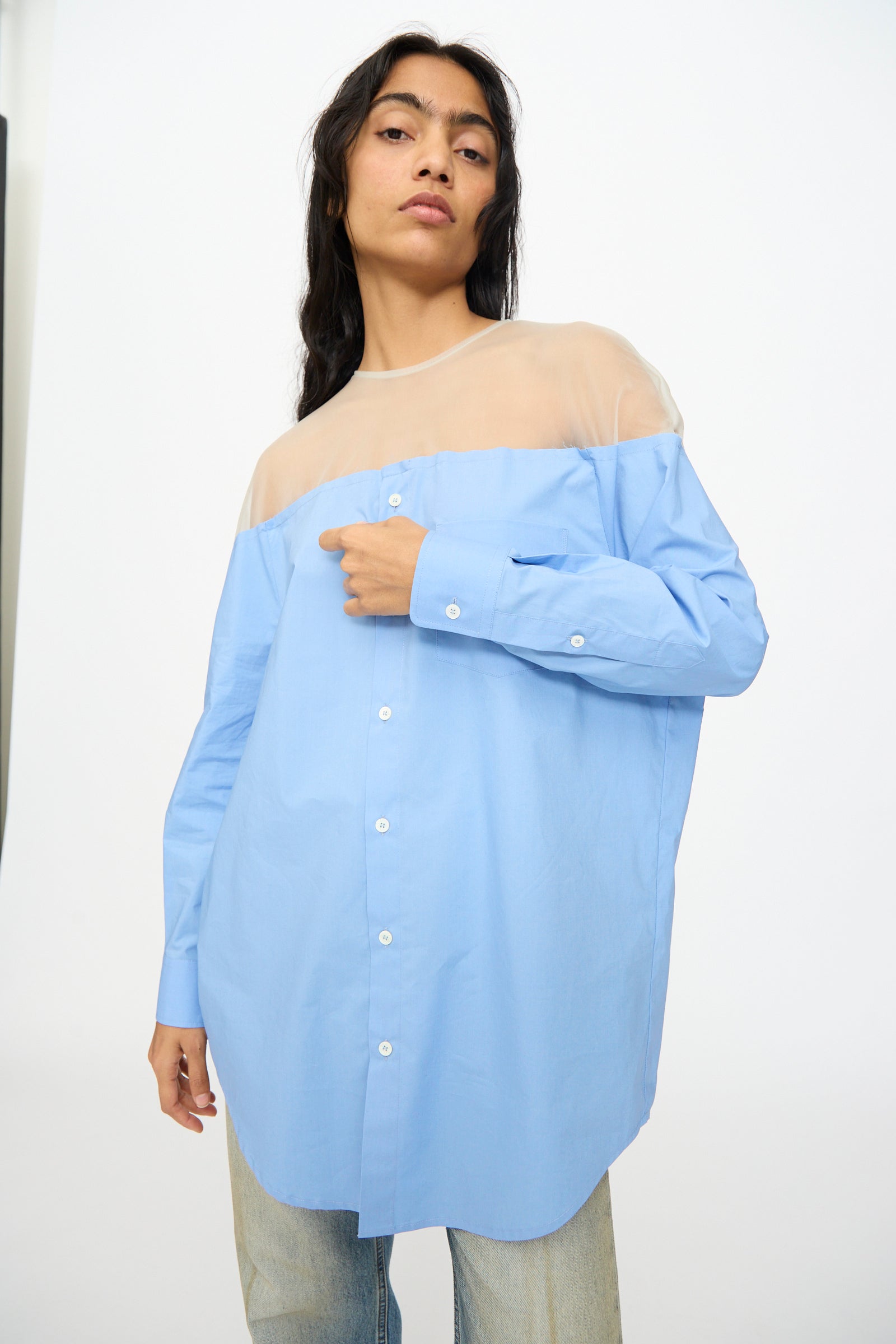 A person wears the MM6 Long Sleeved Top in Sky Blue featuring a sheer beige upper panel, paired with light blue jeans, standing against a plain background.
