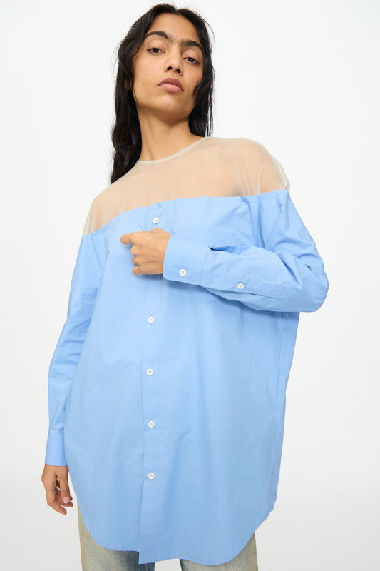 A person wears the MM6 Long Sleeved Top in Sky Blue featuring a sheer beige upper panel, paired with light blue jeans, standing against a plain background.