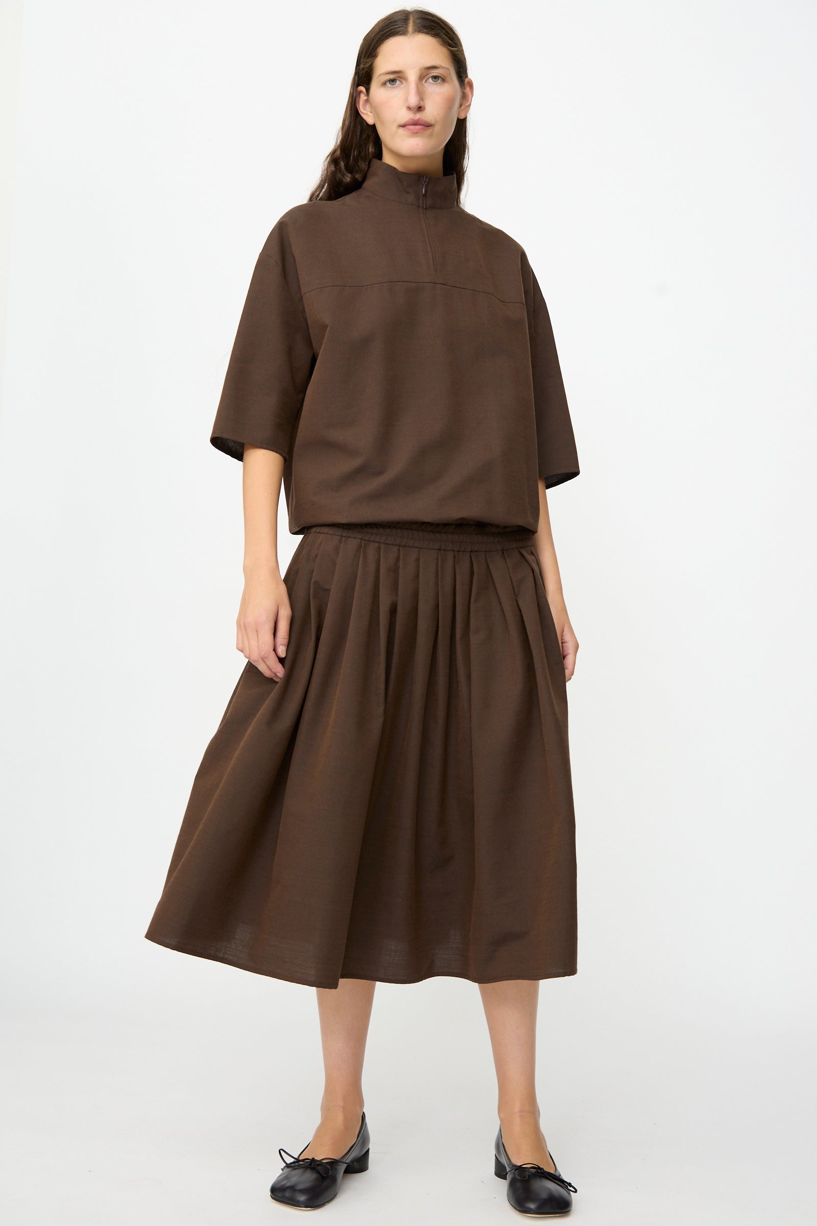 A woman stands against a plain background, wearing the MM6 Maxi Dress in Brown.