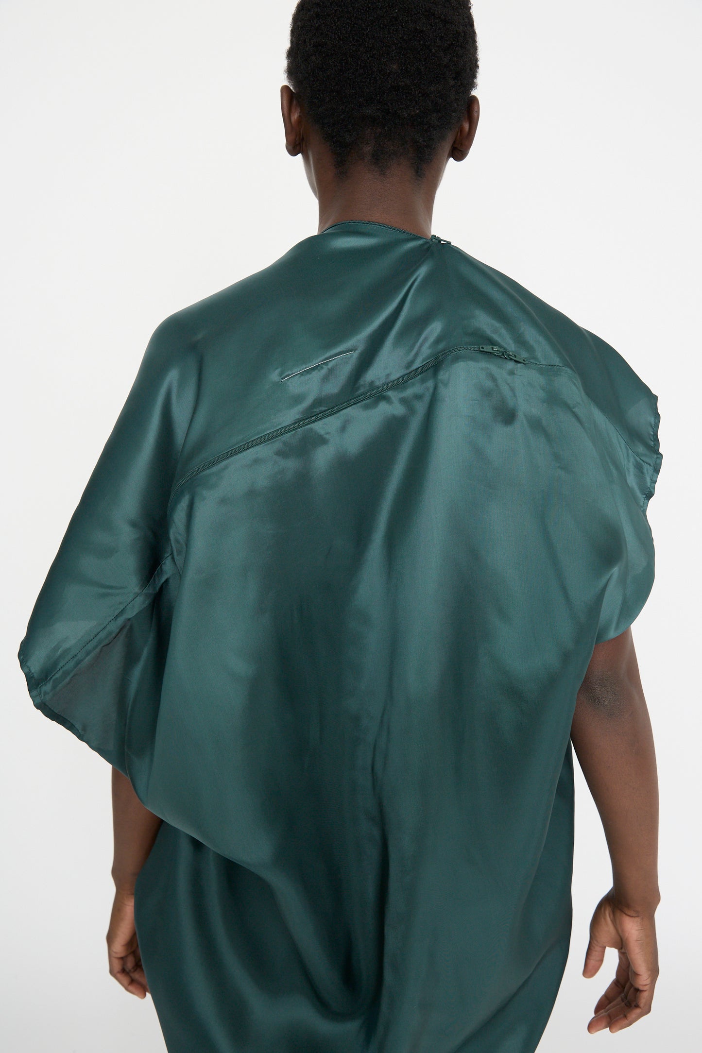 A person draped in an MM6 Maxi Dress in Green stands with their back to the camera against a plain white background.