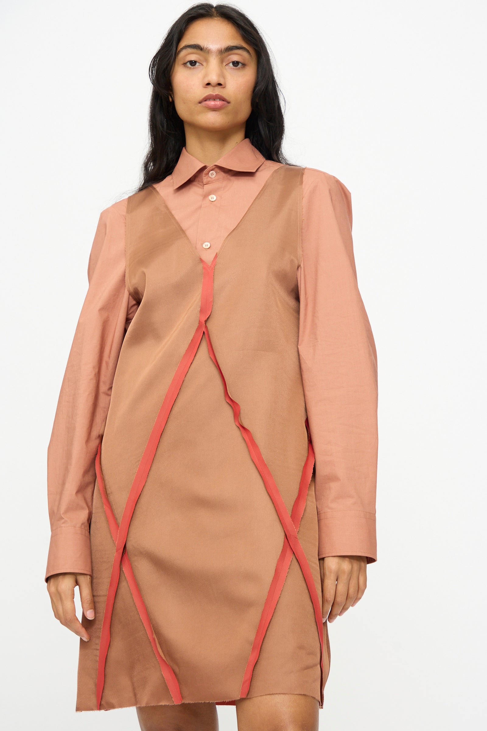 A woman wears the MM6 Midi Dress in Light Brown, a V-neck shirt dress with red trim details made from an acetate blend, standing against a plain white background.