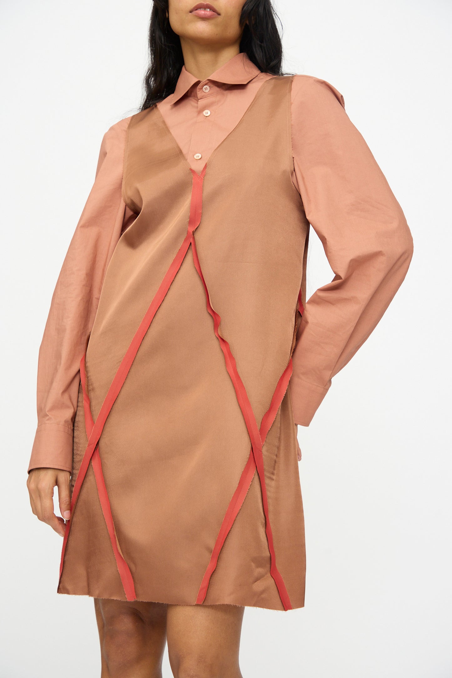 A woman models the MM6 Midi Dress in Light Brown, featuring a sleeveless acetate blend with red trim, layered over a pink collared shirt, set against a plain white background.