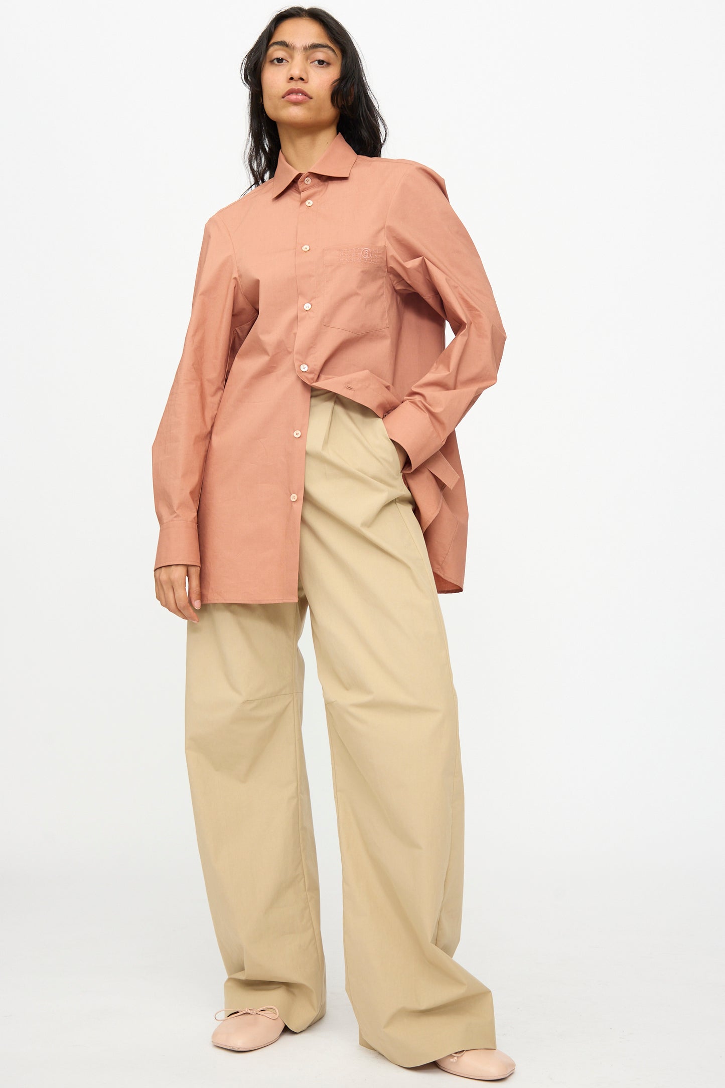 A person wearing a long-sleeve, button-up pink shirt and MM6 Pants in Beige stands against a plain white background.