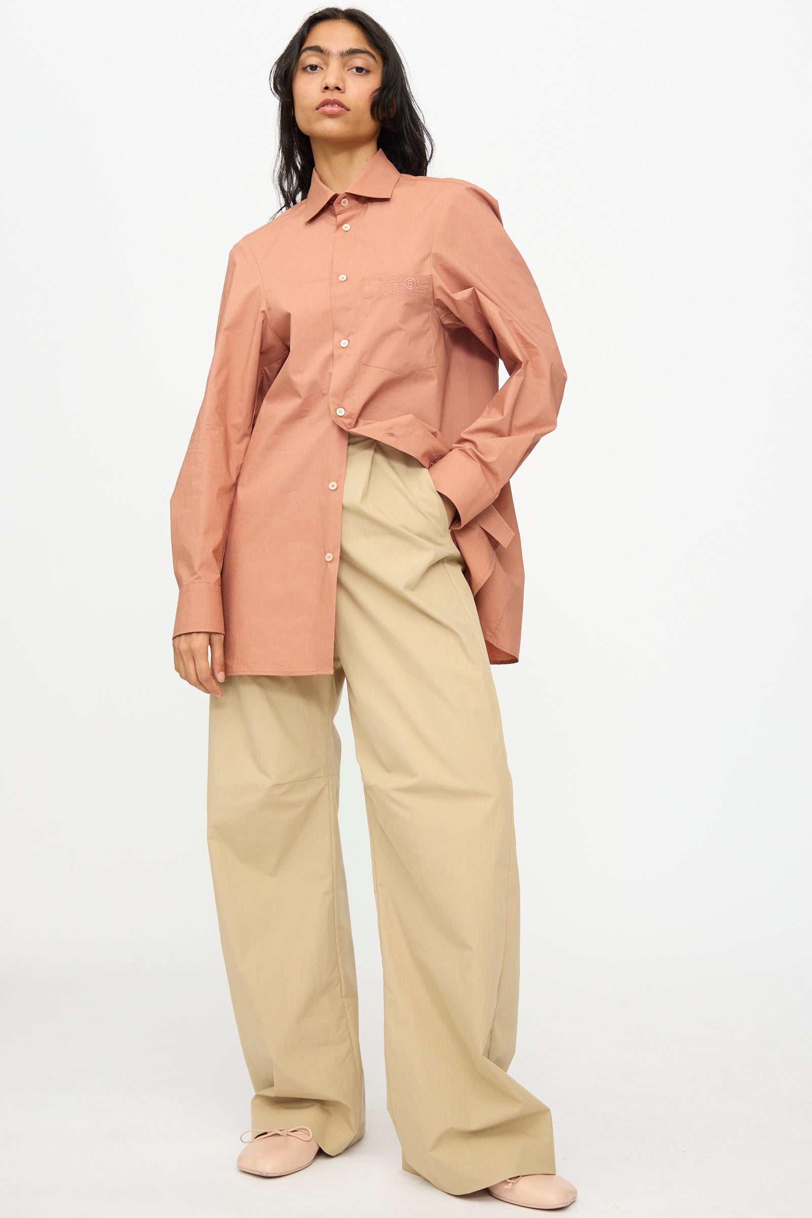 A person wearing a long-sleeve, button-up pink shirt and MM6 Pants in Beige stands against a plain white background.