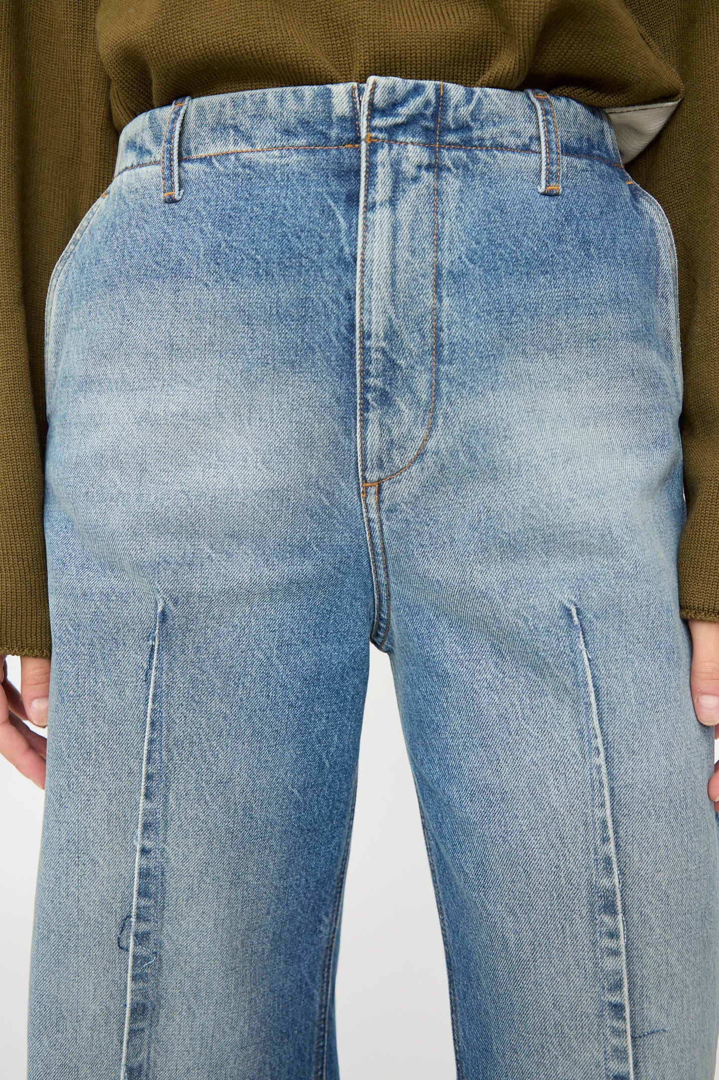 A person wearing MM6’s Pants in Blue, featuring a high-waisted cut and front seams, paired with a green ribbed sweater. The relaxed fit and faded denim create a casual, effortless look, as shown from waist to mid-thigh.