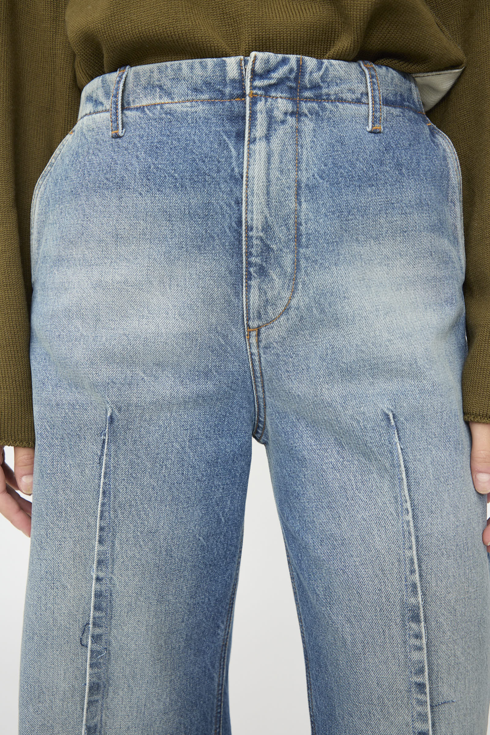 A person wearing MM6’s Pants in Blue, featuring a high-waisted cut and front seams, paired with a green ribbed sweater. The relaxed fit and faded denim create a casual, effortless look, as shown from waist to mid-thigh.