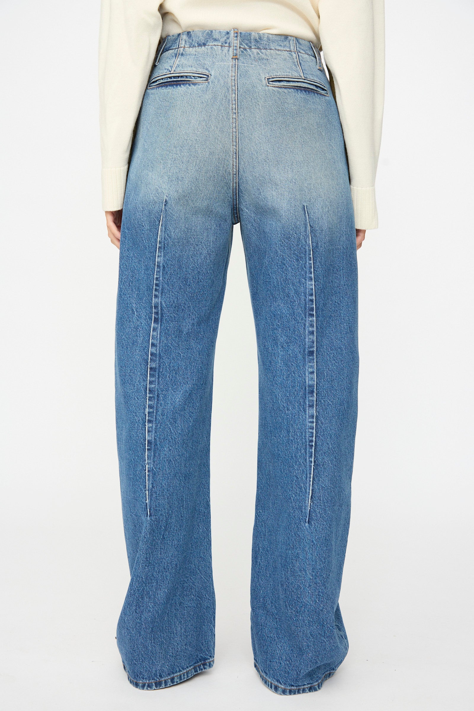 Model is seen from the back wearing MM6’s Pants in Blue, featuring a relaxed fit, high-waisted wide-leg silhouette with vertical seams and two welt pockets at the rear, crafted from subtly faded denim.