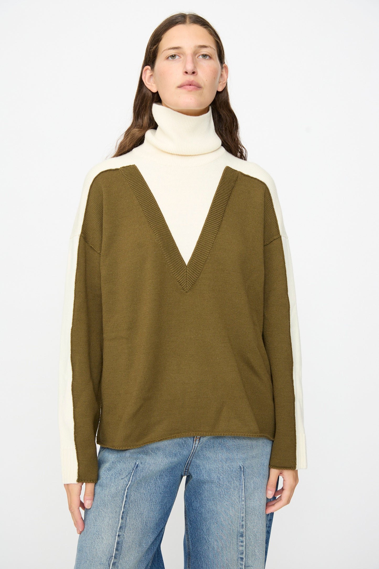 Wearing the MM6 Pullover in Off White-khaki, which features a color-blocked olive green body and cream sleeves with a cozy wool turtleneck, styled with blue jeans against a plain white background.
