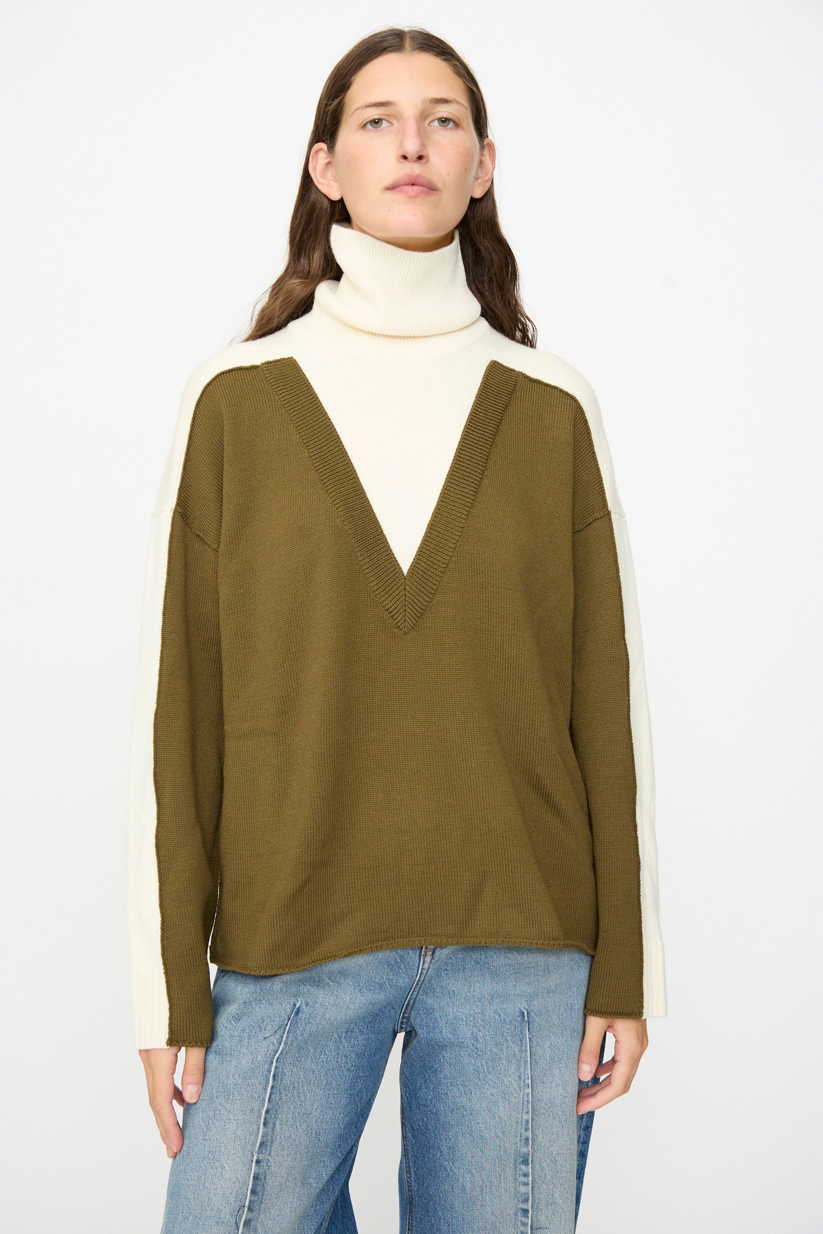 Wearing the MM6 Pullover in Off White-khaki, which features a color-blocked olive green body and cream sleeves with a cozy wool turtleneck, styled with blue jeans against a plain white background.